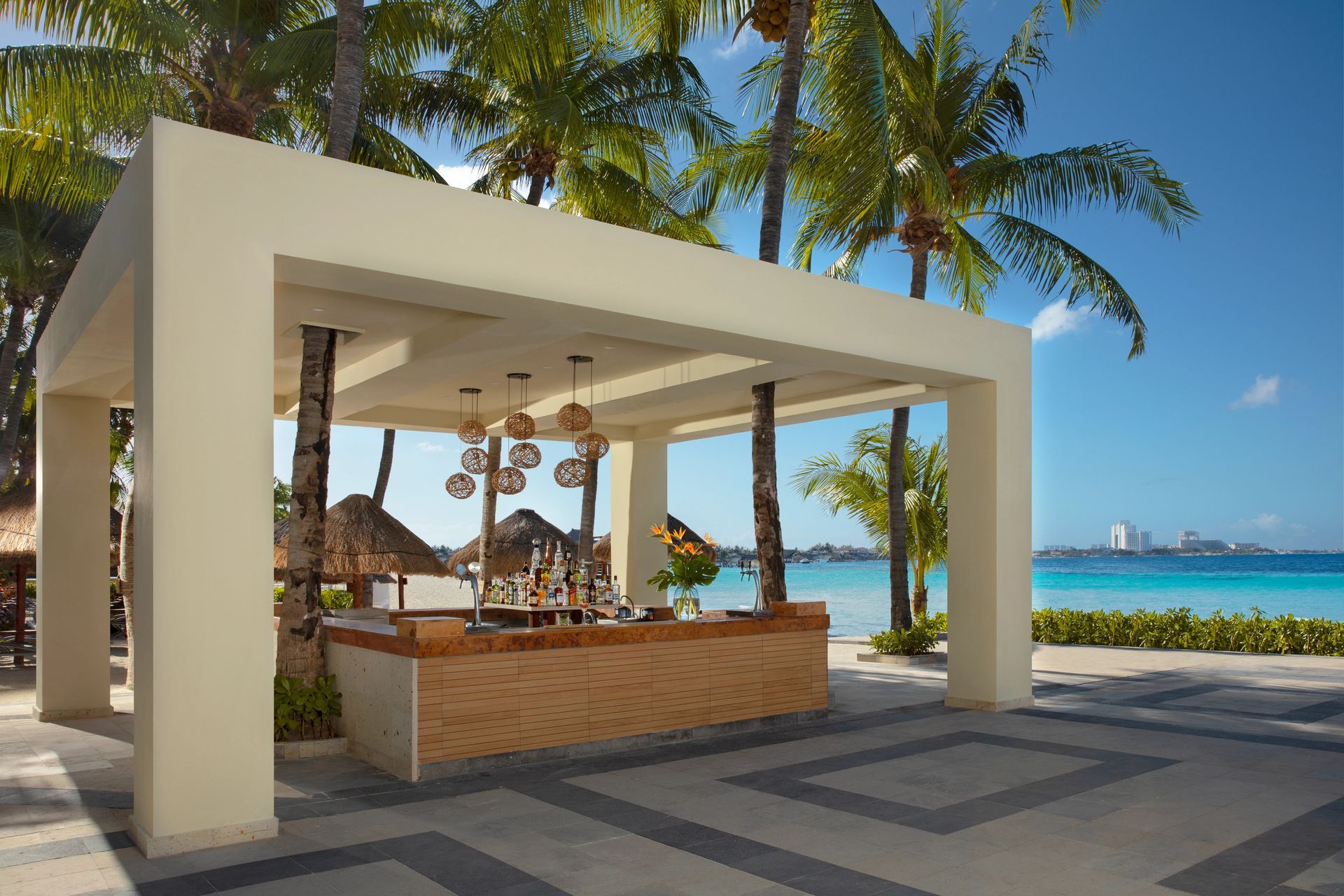 A beach bar with palm trees and the ocean in the background at Dreams Sands Resorts & Spas in Cancun.