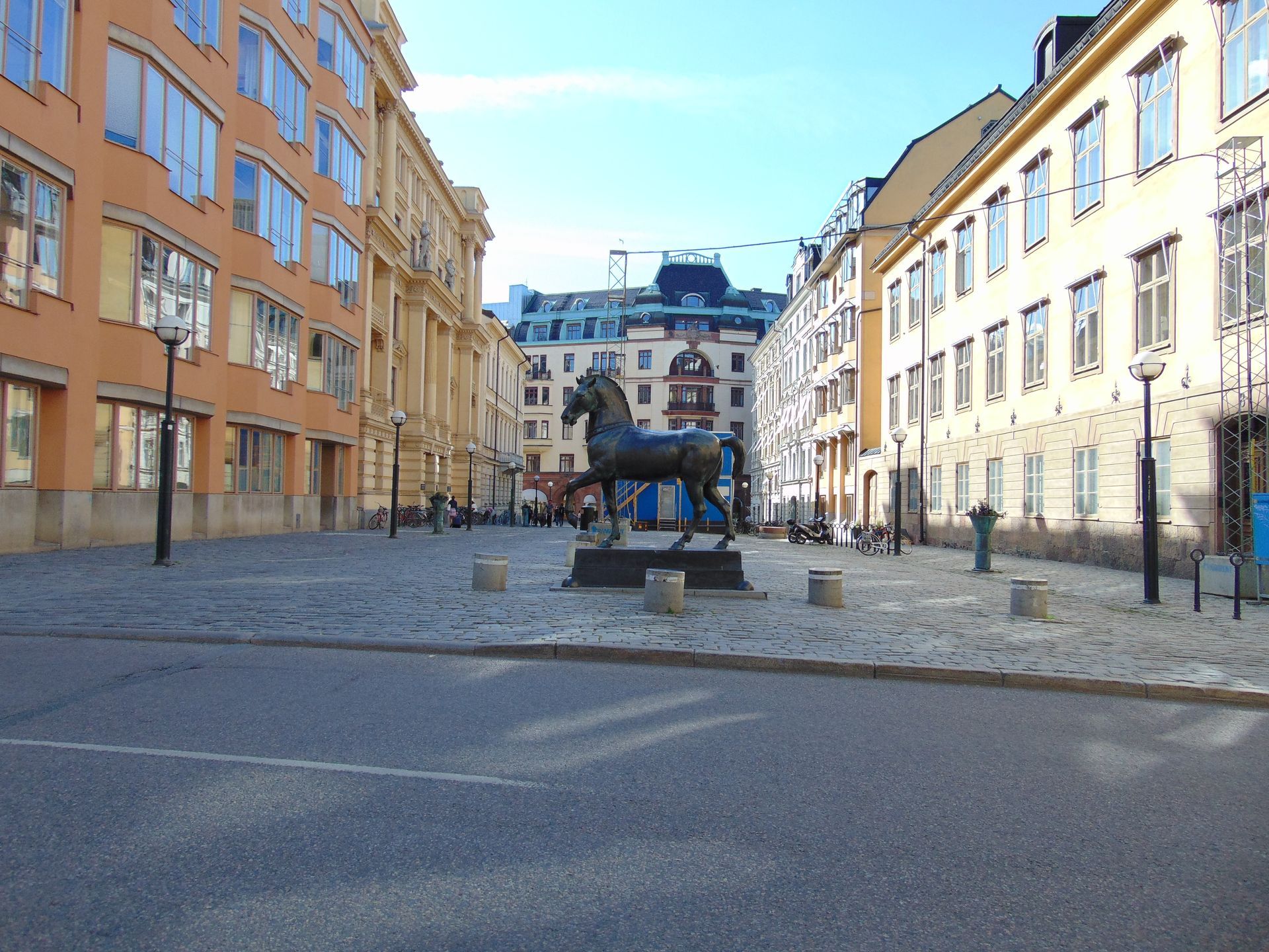 Bronze horse statue in cobblestone square, flanked by buildings. Sunny day.