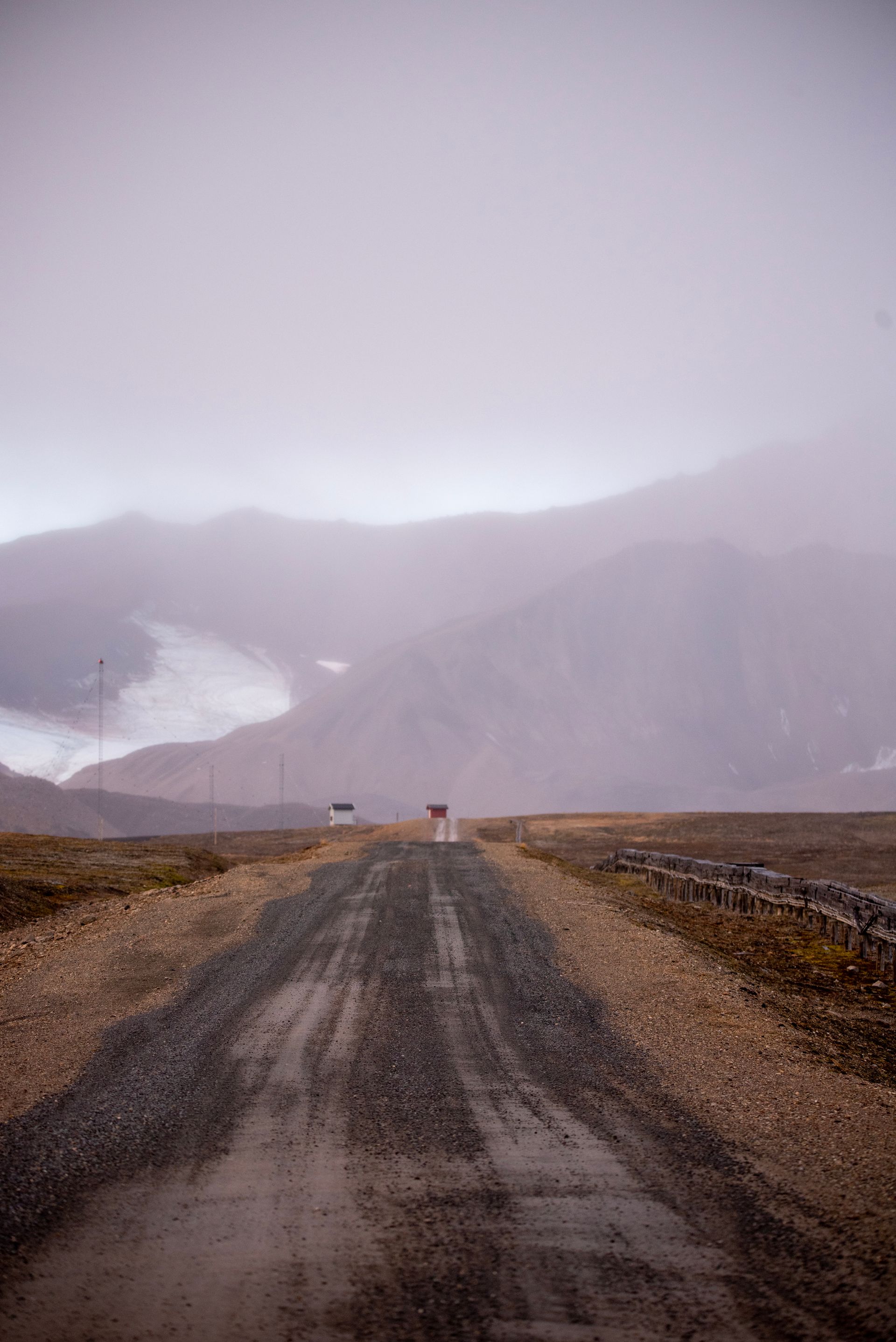 A dirt road going through a foggy landscape with mountains in the background in Svalbard.