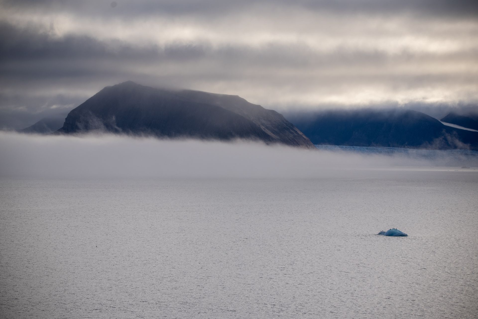 A large iceberg in the middle of a snowy field with mountains in the background in Svalbard.