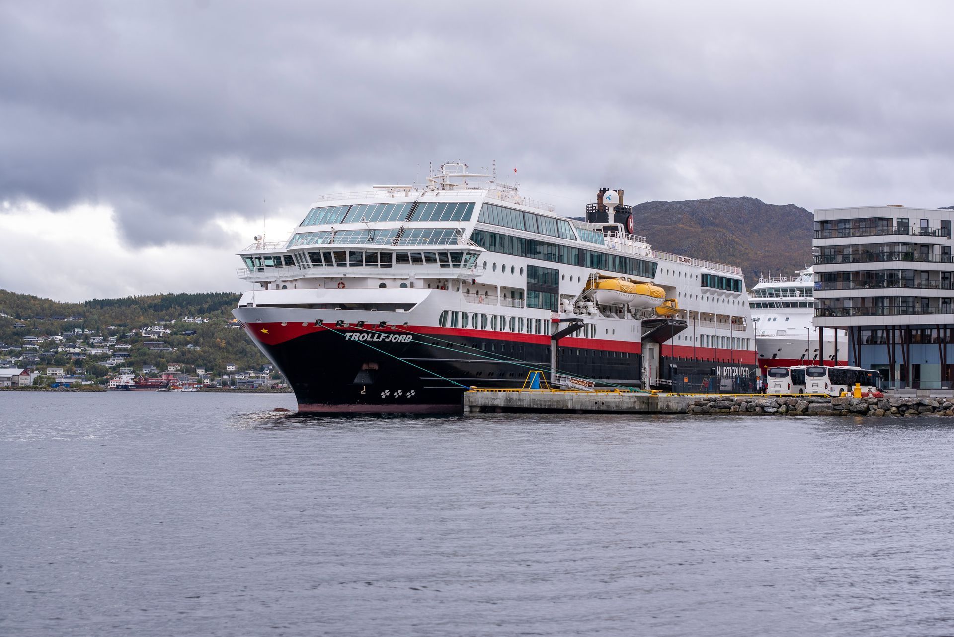 A large Hurtigruten cruise ship is docked in a harbor in Svalbard.