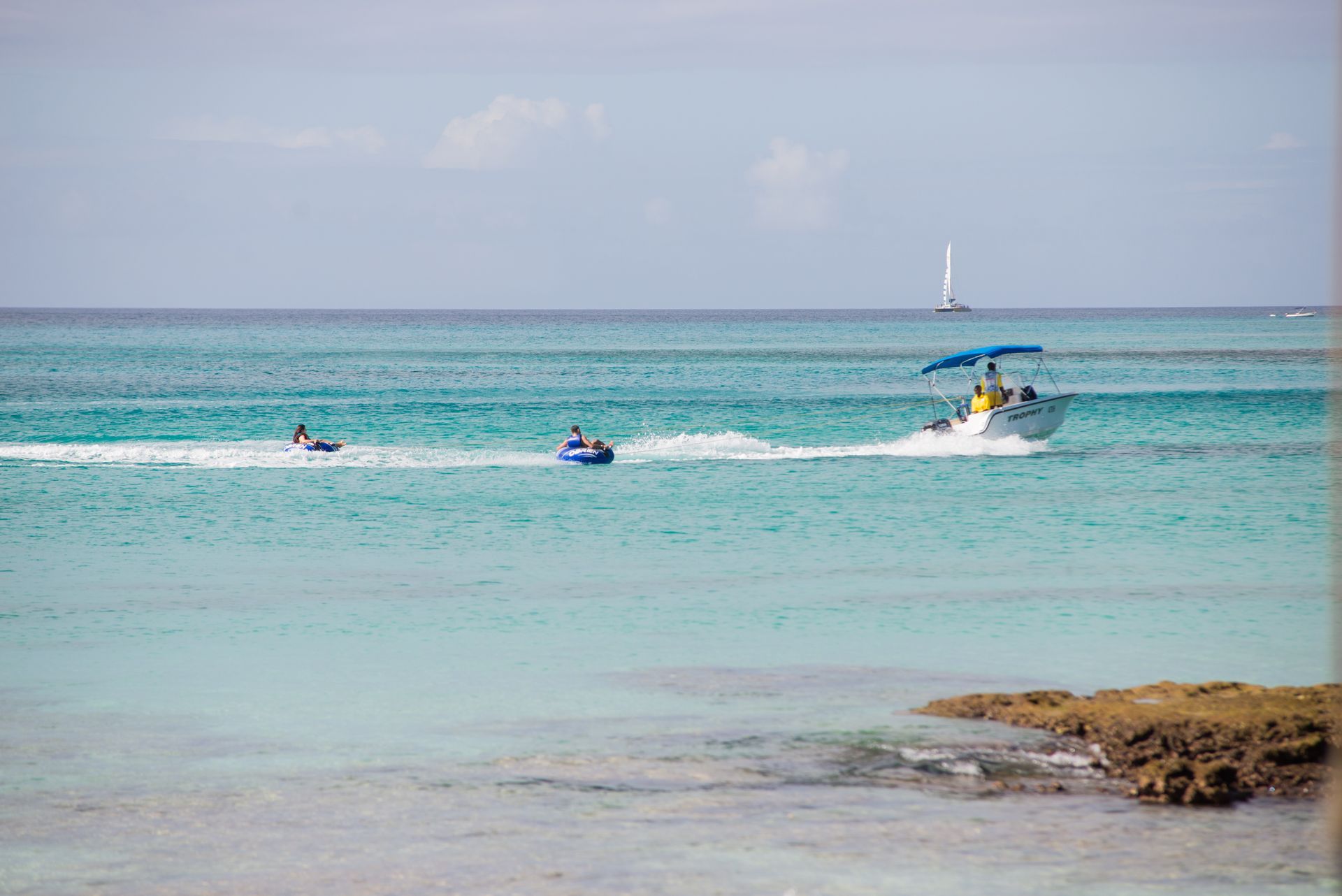 Boat pulling two people on inner tubes in turquoise ocean water.