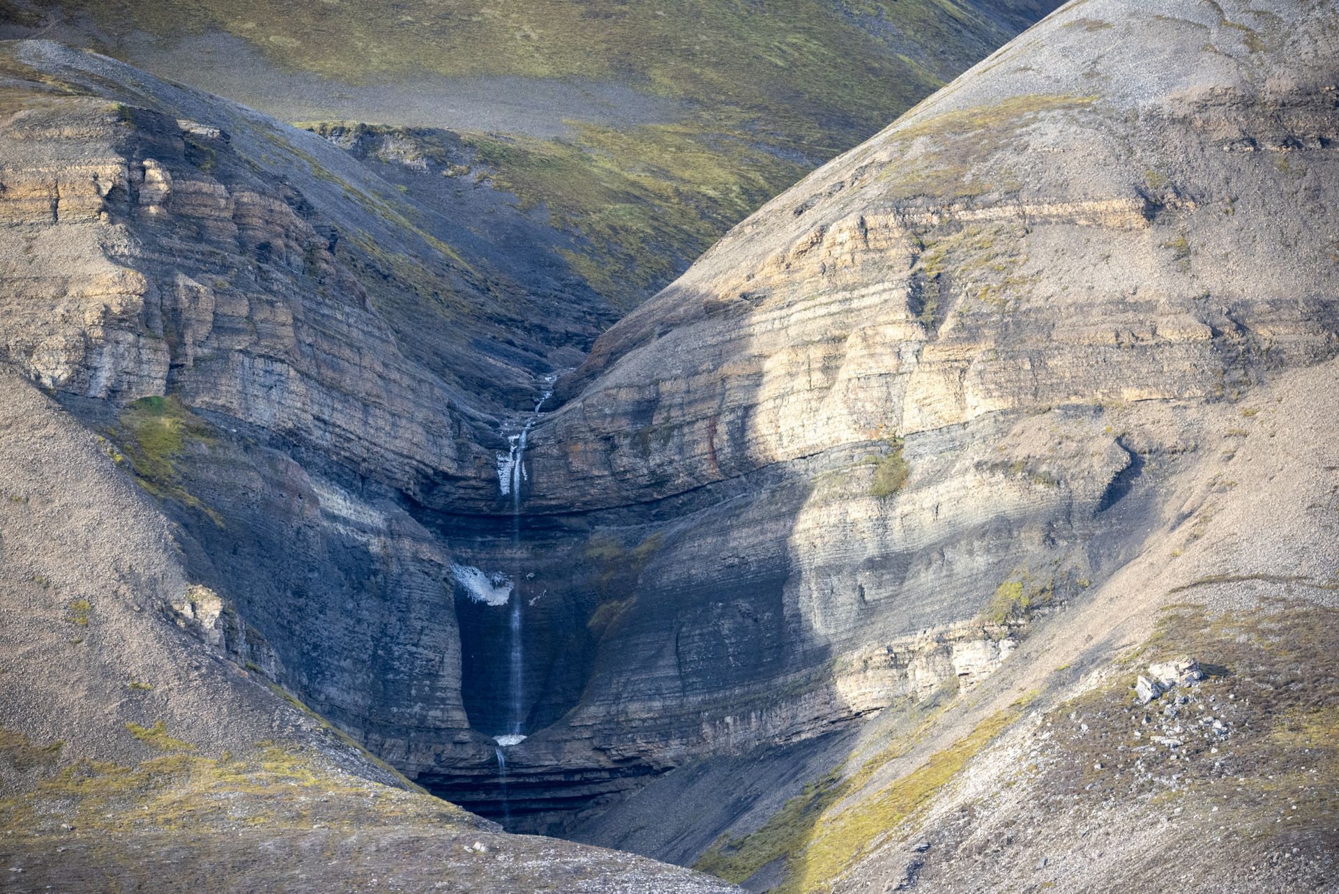 An aerial view of a waterfall in the middle of a valley in Svalbard.