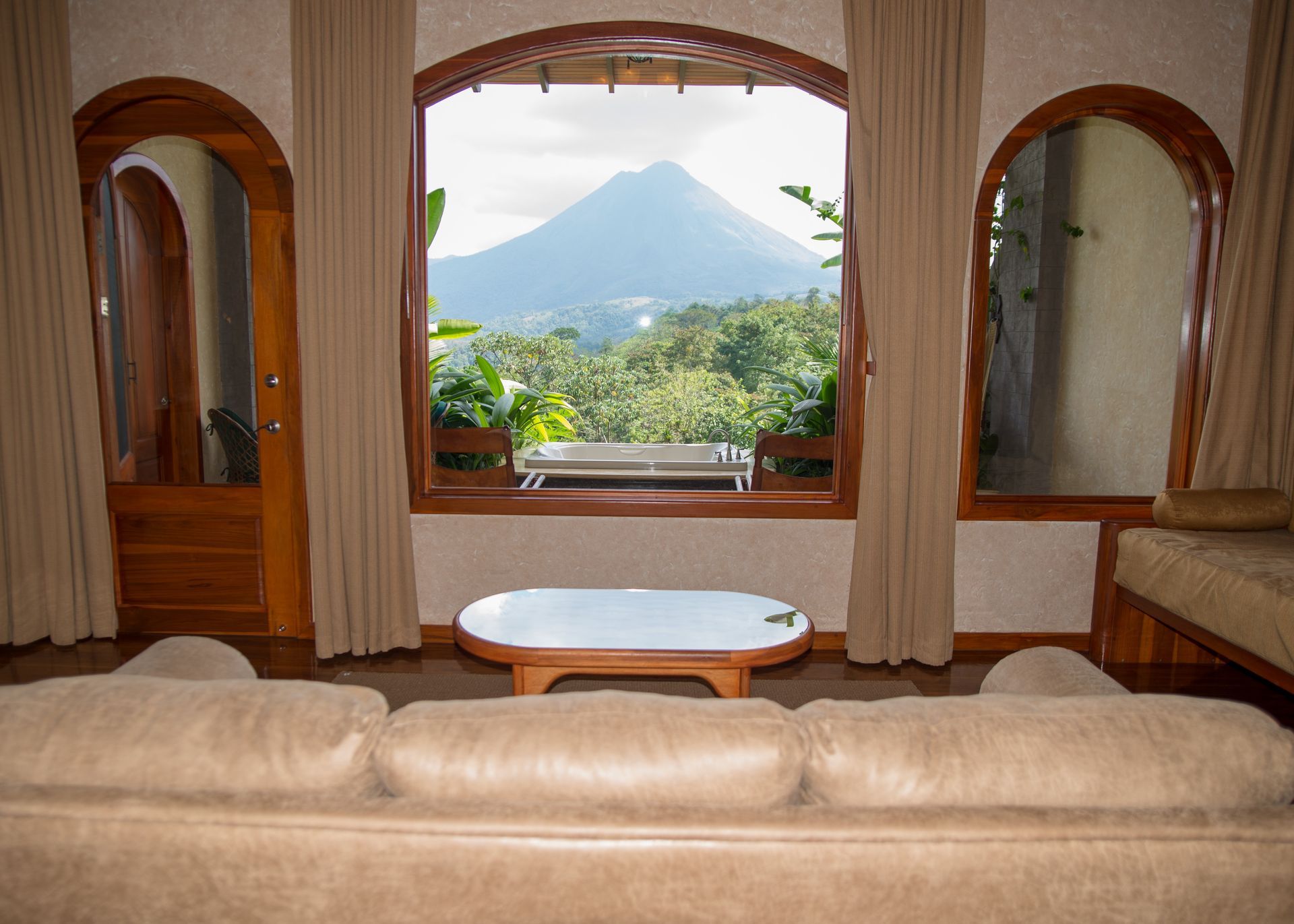 Cozy interior with a large window framing a mountain view, couch, table, and arched doorways.