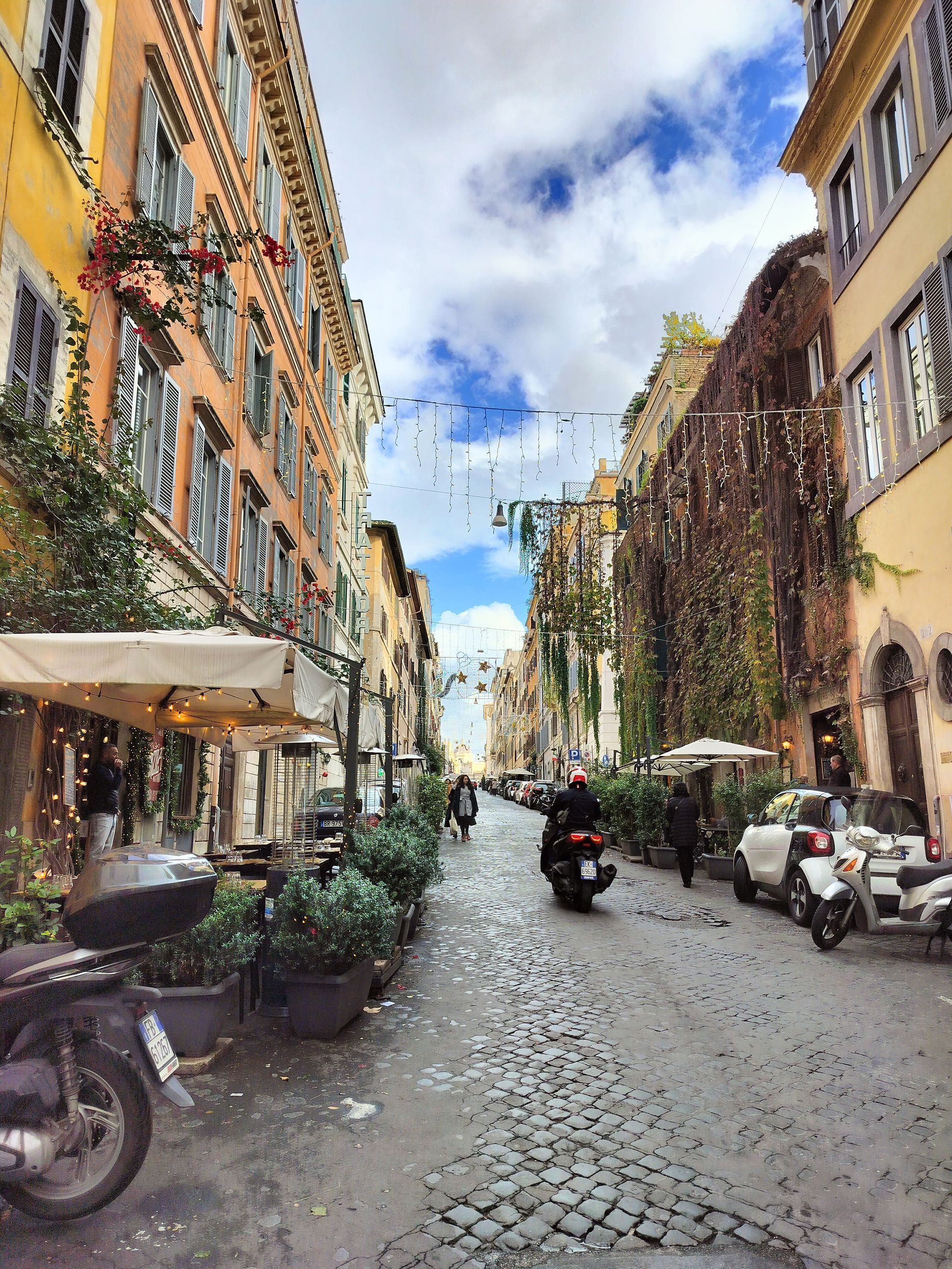 Cobblestone street in Rome lined with buildings, cafe, and scooter.