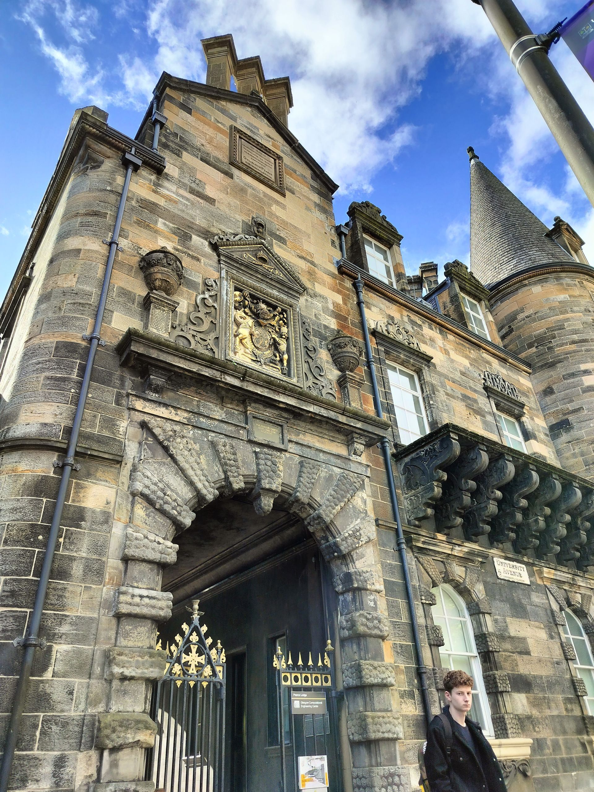 Stone arched entrance to a historic building with detailed carvings, blue sky. A person stands nearby.