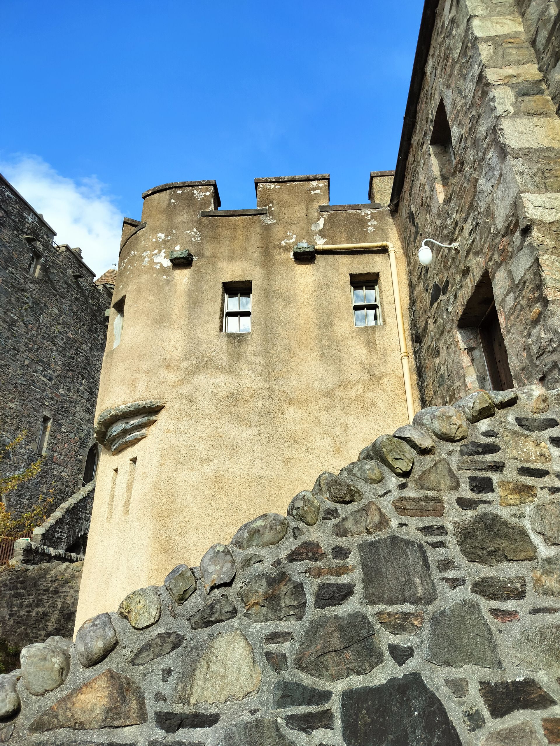 Stone castle tower against a blue sky, viewed from a stone wall below.