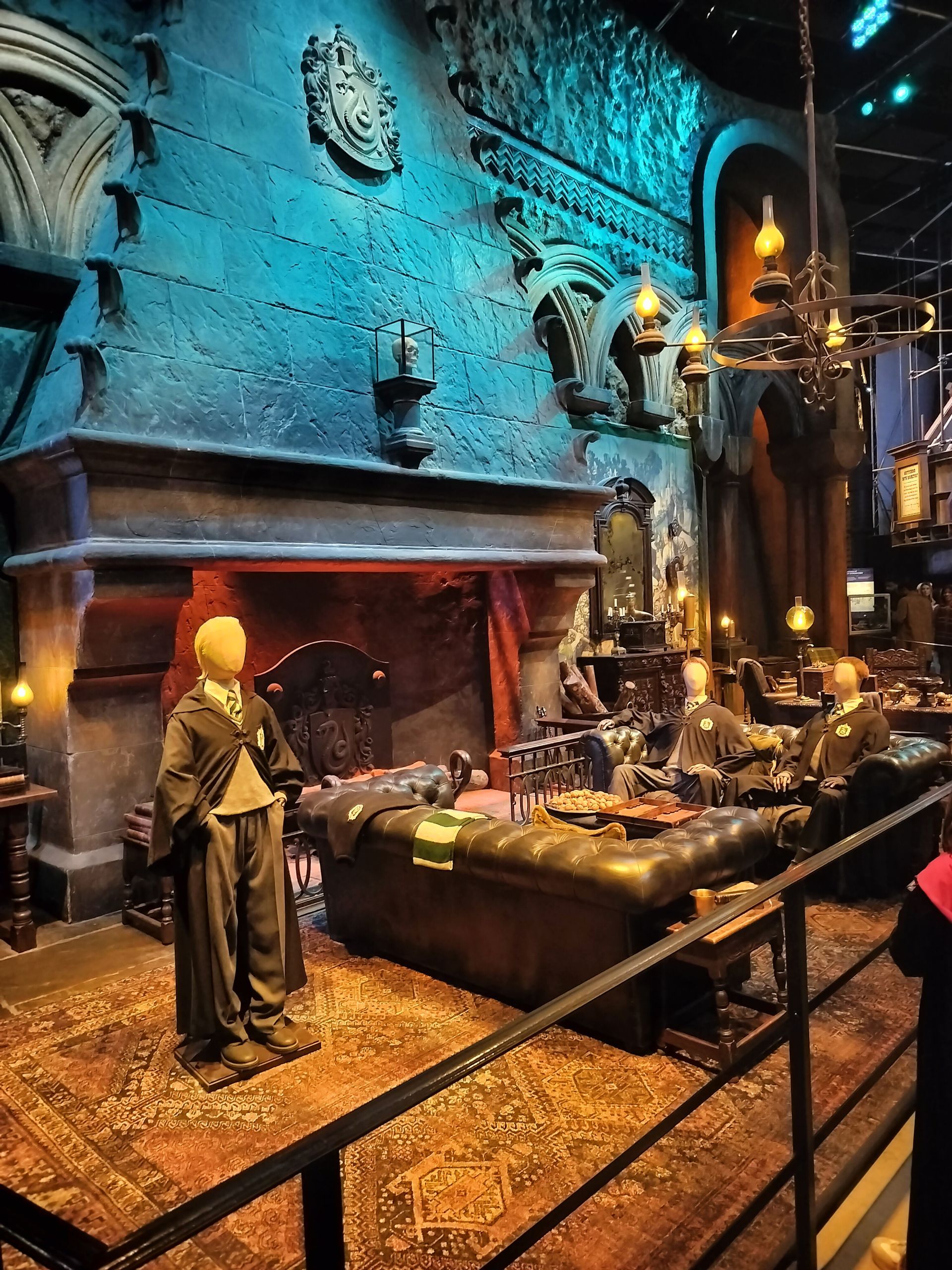 A wizarding classroom set from Harry Potter. A mannequin in robes stands before a fireplace, with a desk and ornate details.