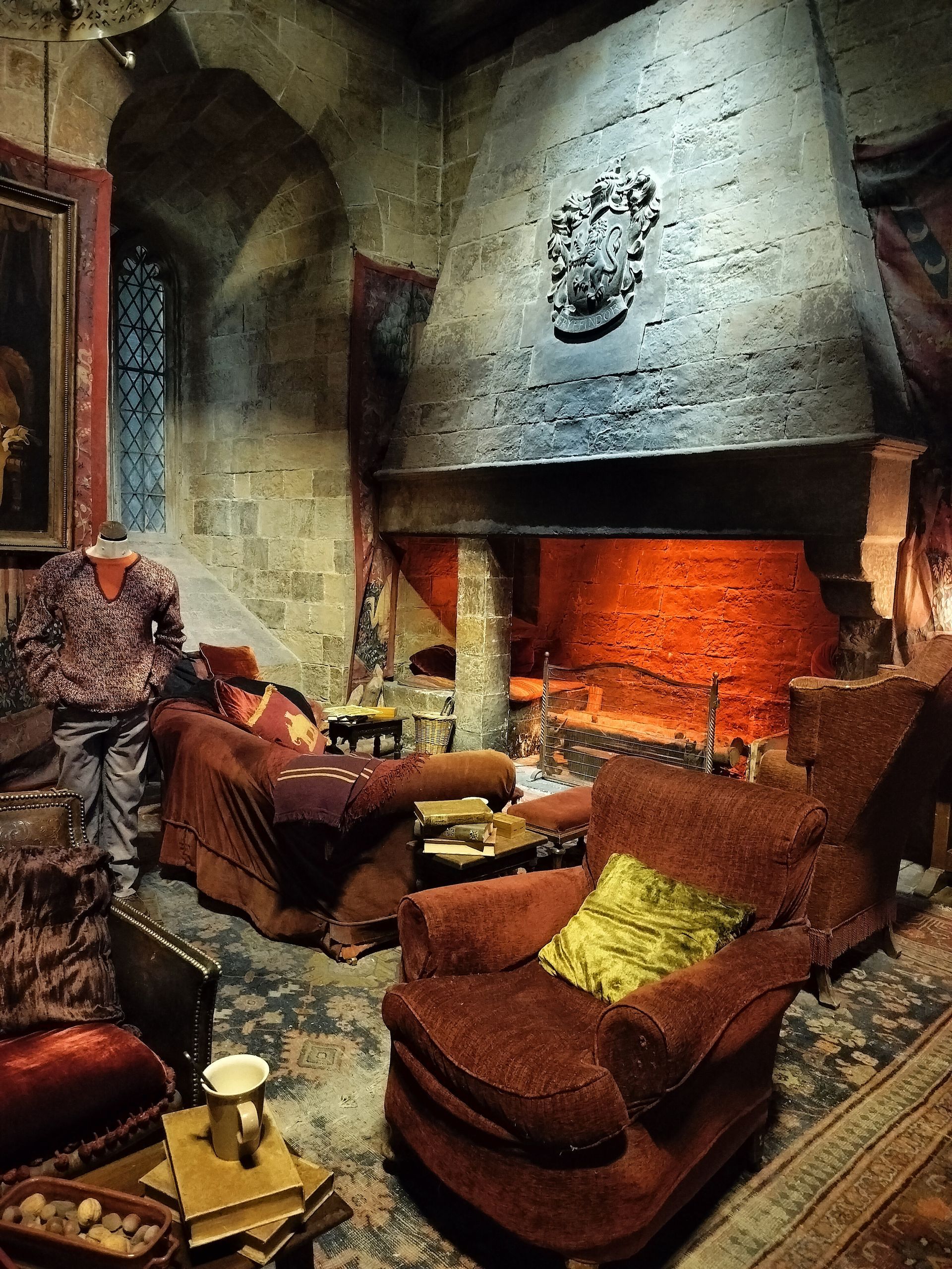 Cozy room with fireplace, armchairs, and tapestry. A headless mannequin stands nearby.