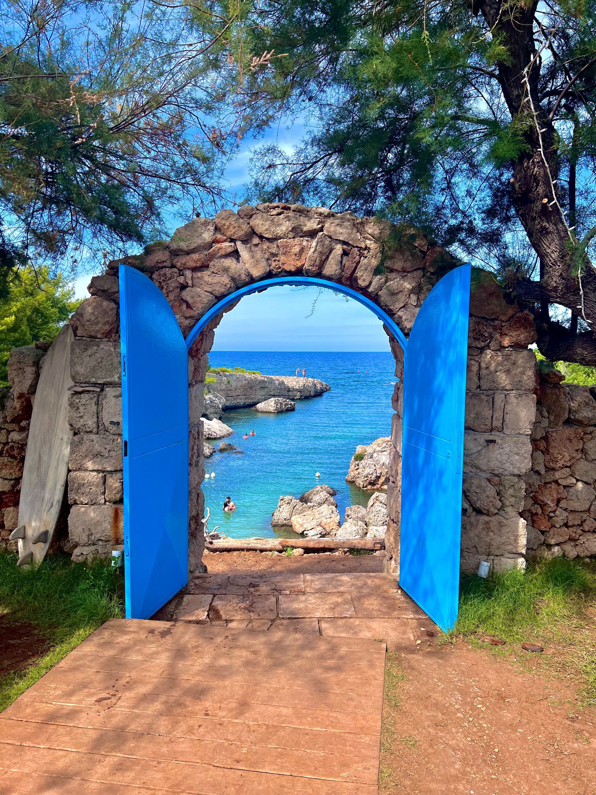 A stone archway with blue doors leading to the ocean in Puglia, Italy.