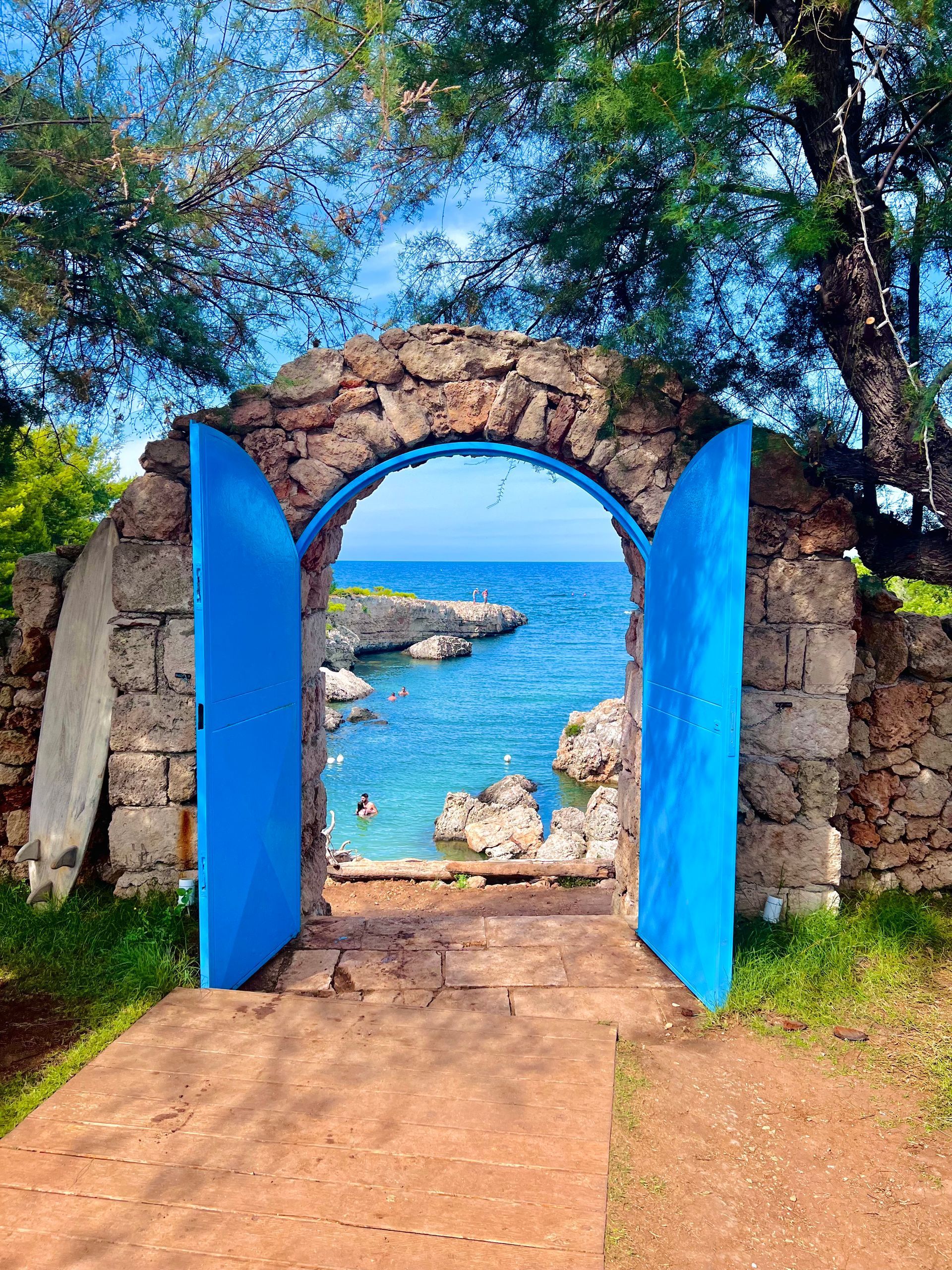 Blue arched doorway opens to a vibrant blue ocean. Stone walls and blue doors frame the view.