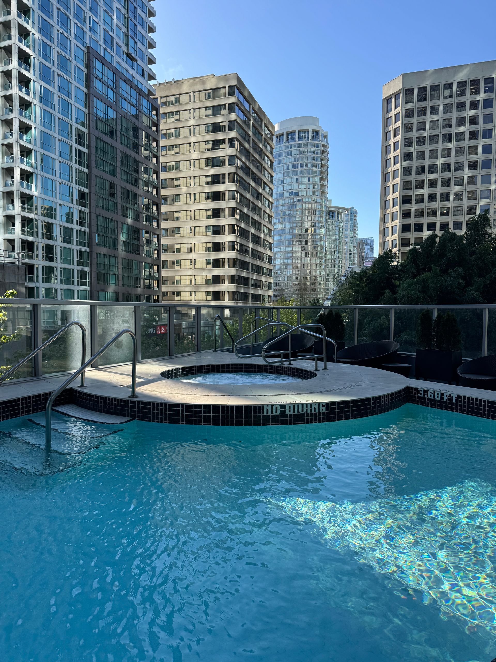Rooftop pool with blue water and lounge area, surrounded by tall modern apartment buildings.