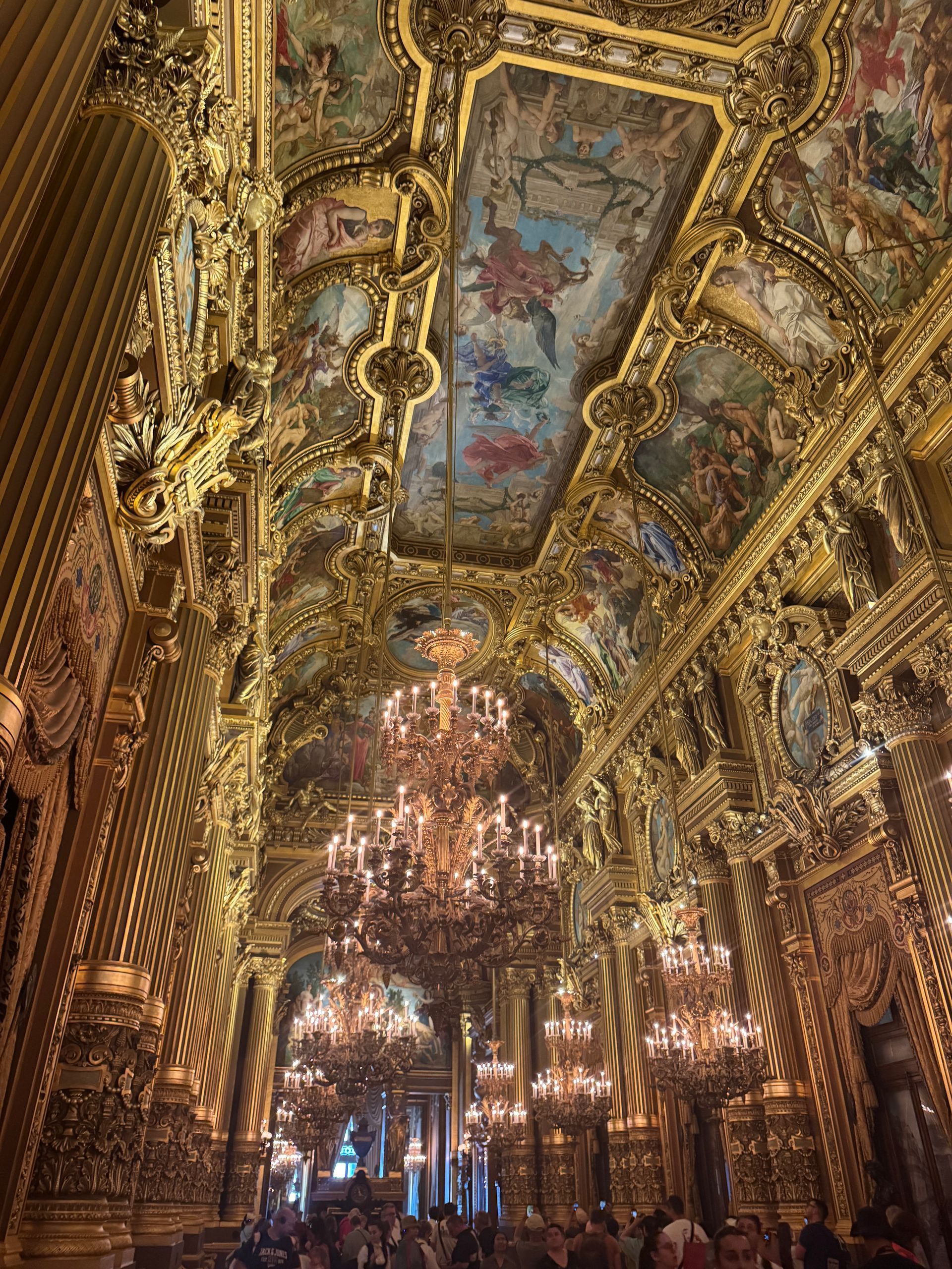 Ornate, gold-adorned opera hall interior with chandeliers and painted ceiling.