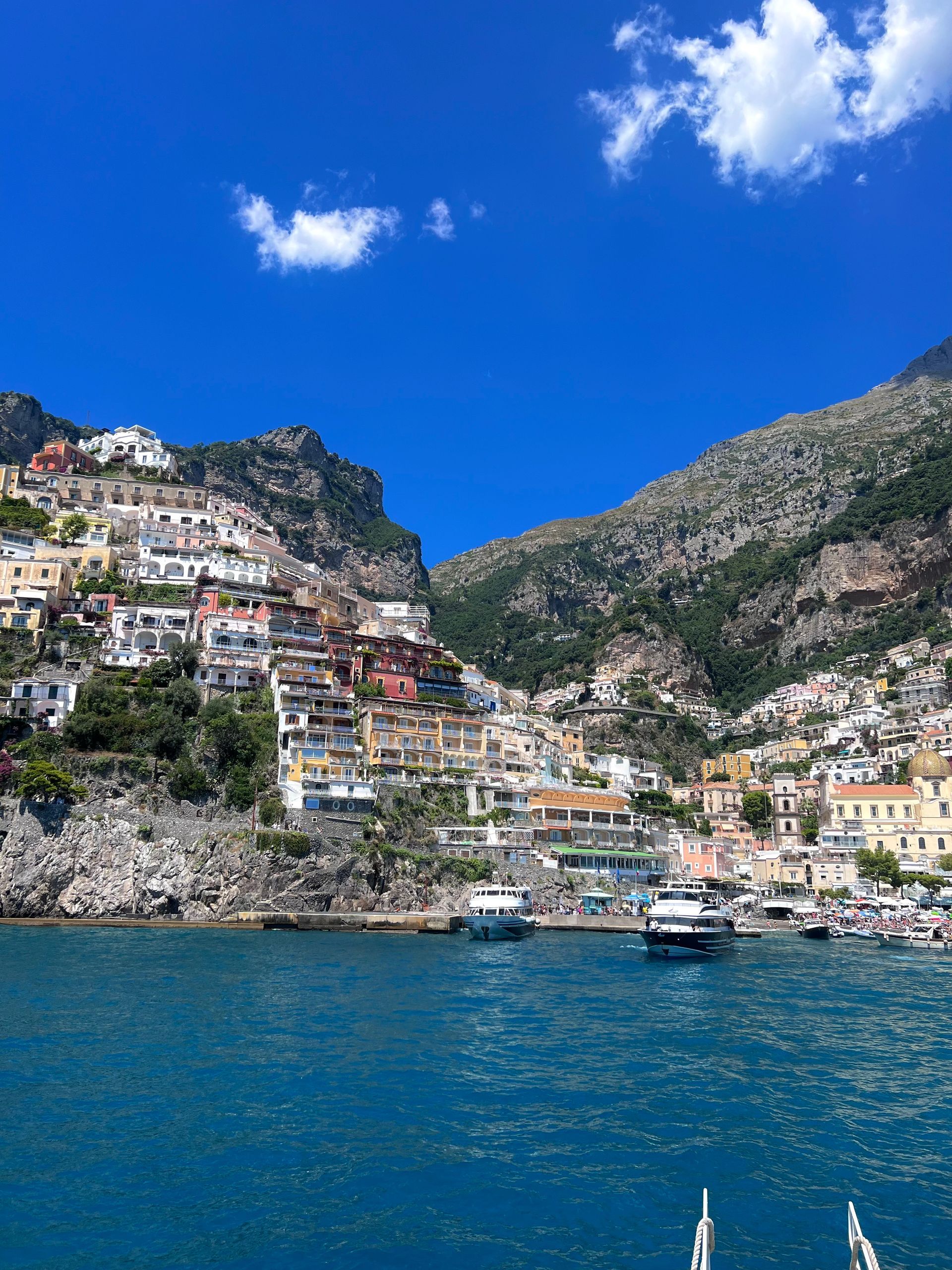 Coastal Italian village of Positano with colorful buildings on a hillside, blue water, and sky.