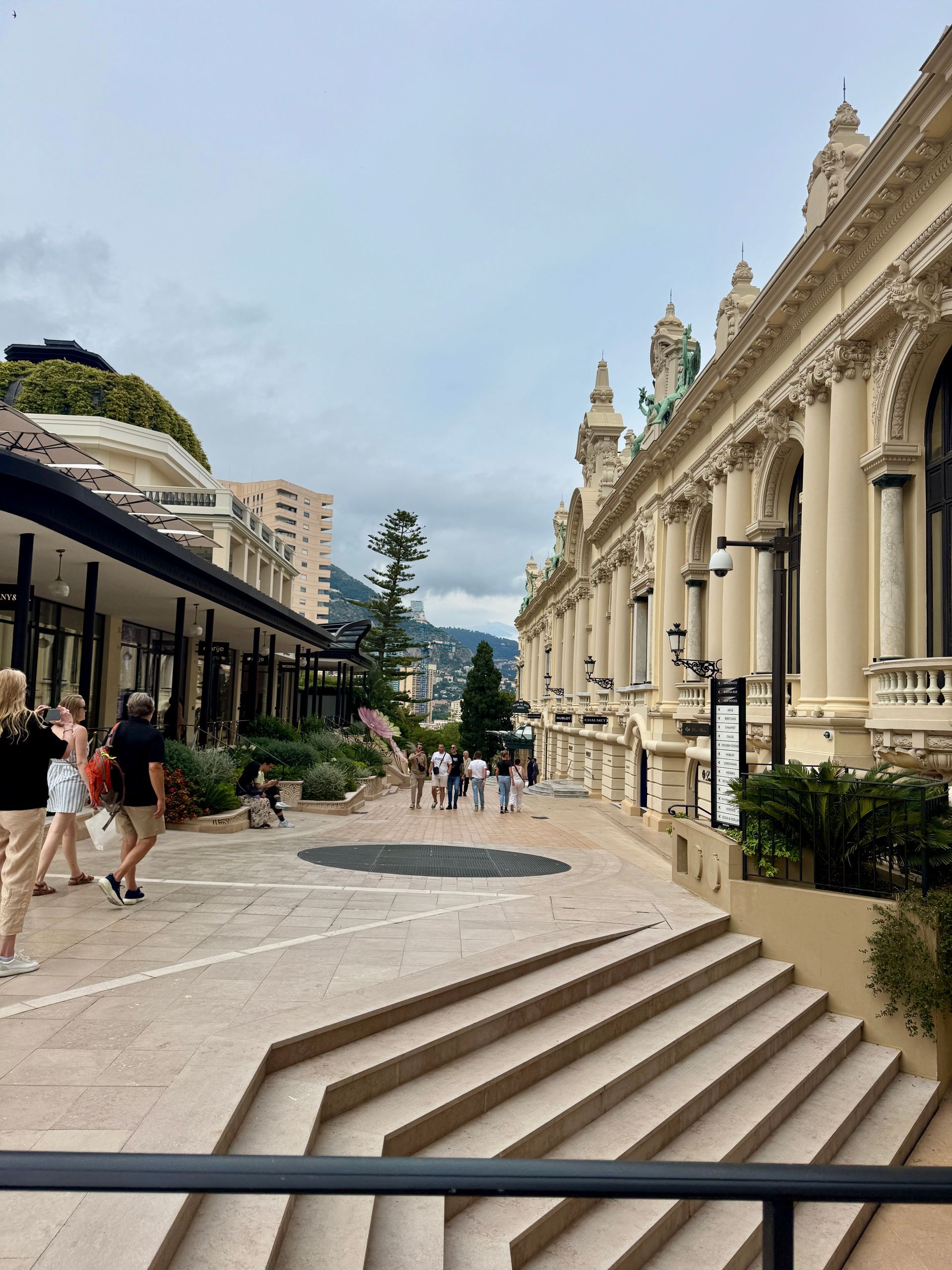 Exterior view of buildings in Monaco, people walking on pathways, cloudy sky.