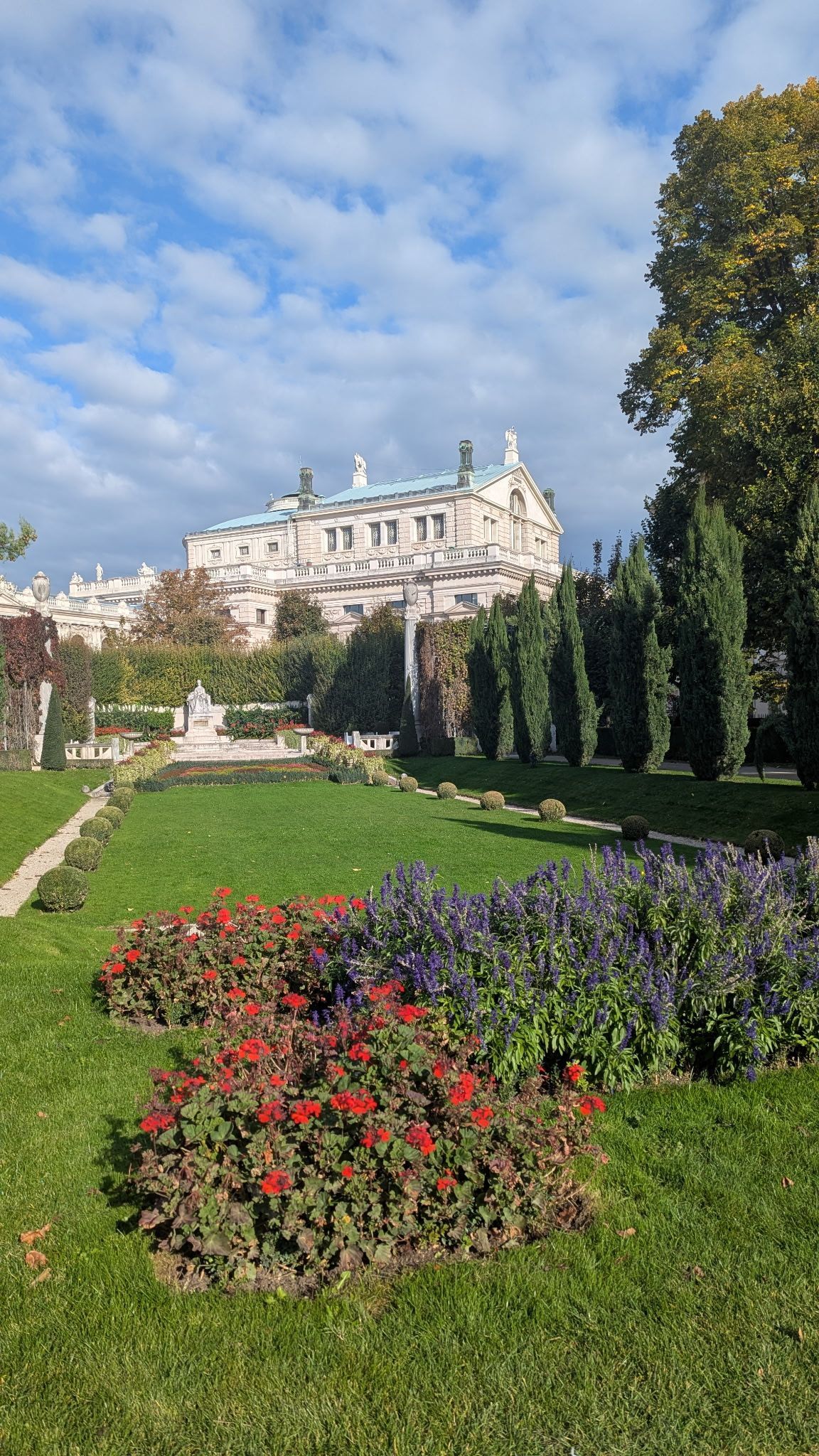 Formal garden with vibrant flowers and ornate building under blue sky.