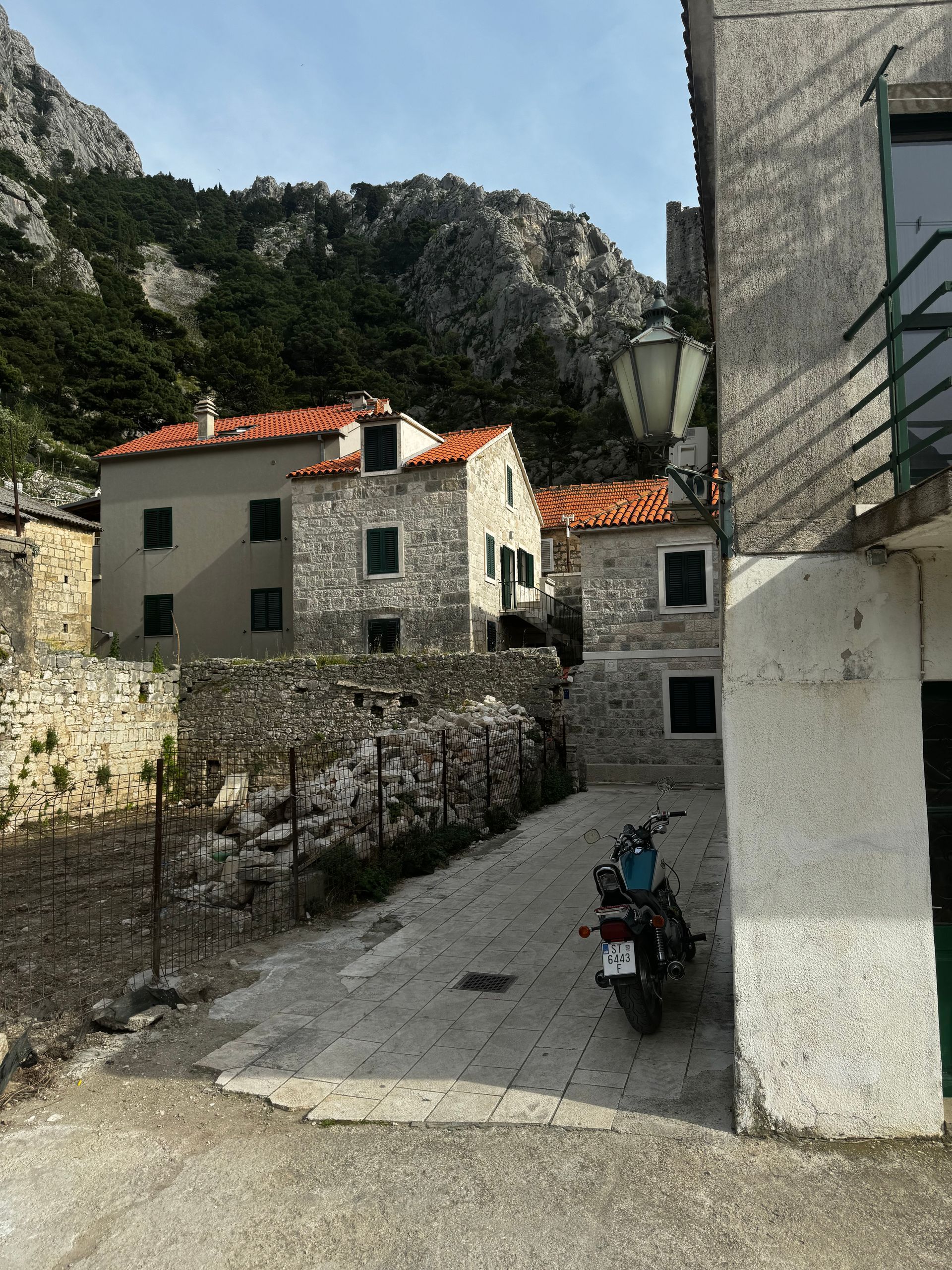 Stone buildings with red-tiled roofs line a narrow street in a mountain village; a parked motorcycle.