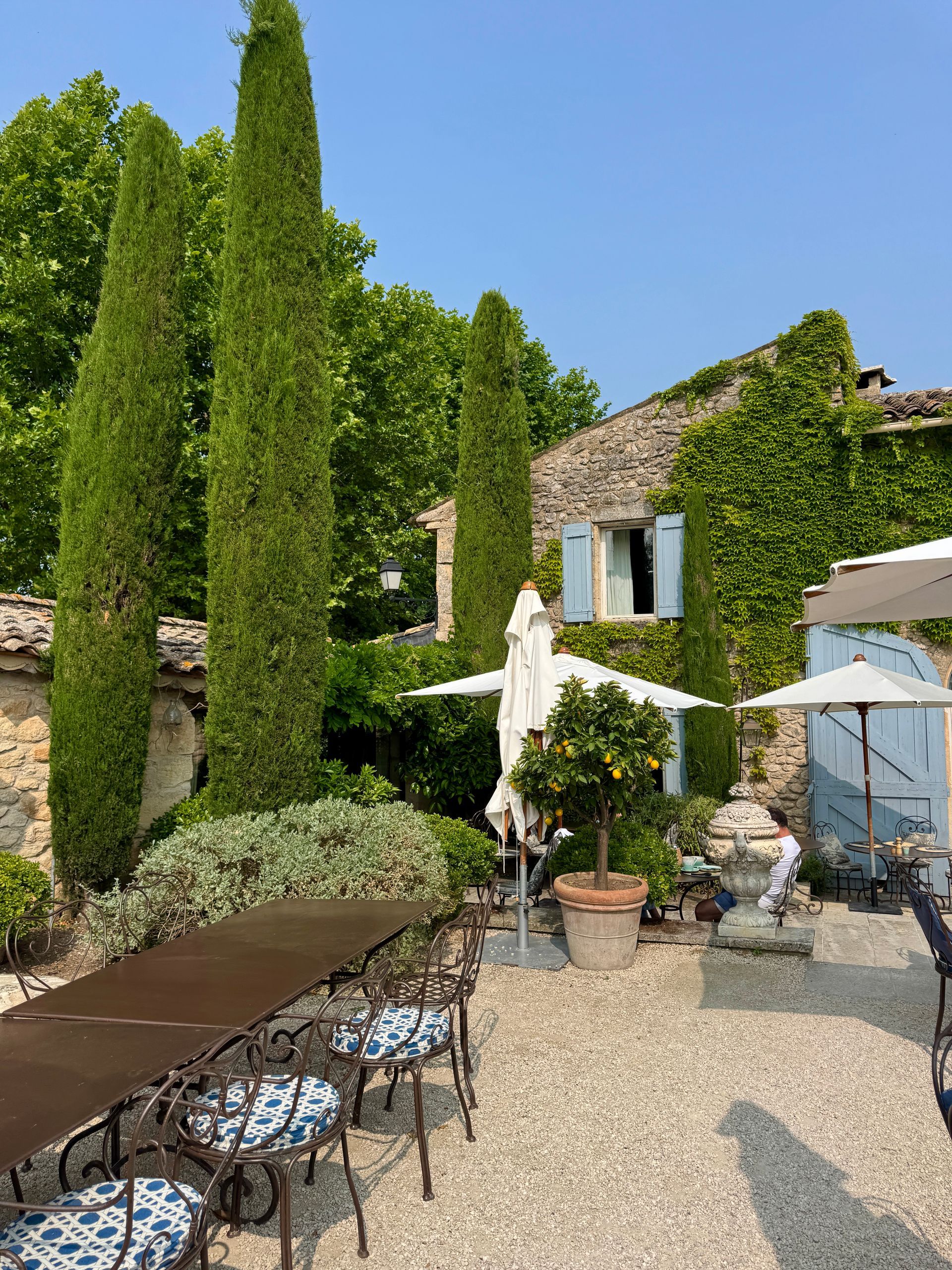 A patio with a table and chairs, and umbrellas in front of a building at La Bastide de Marie in Luberon, France.