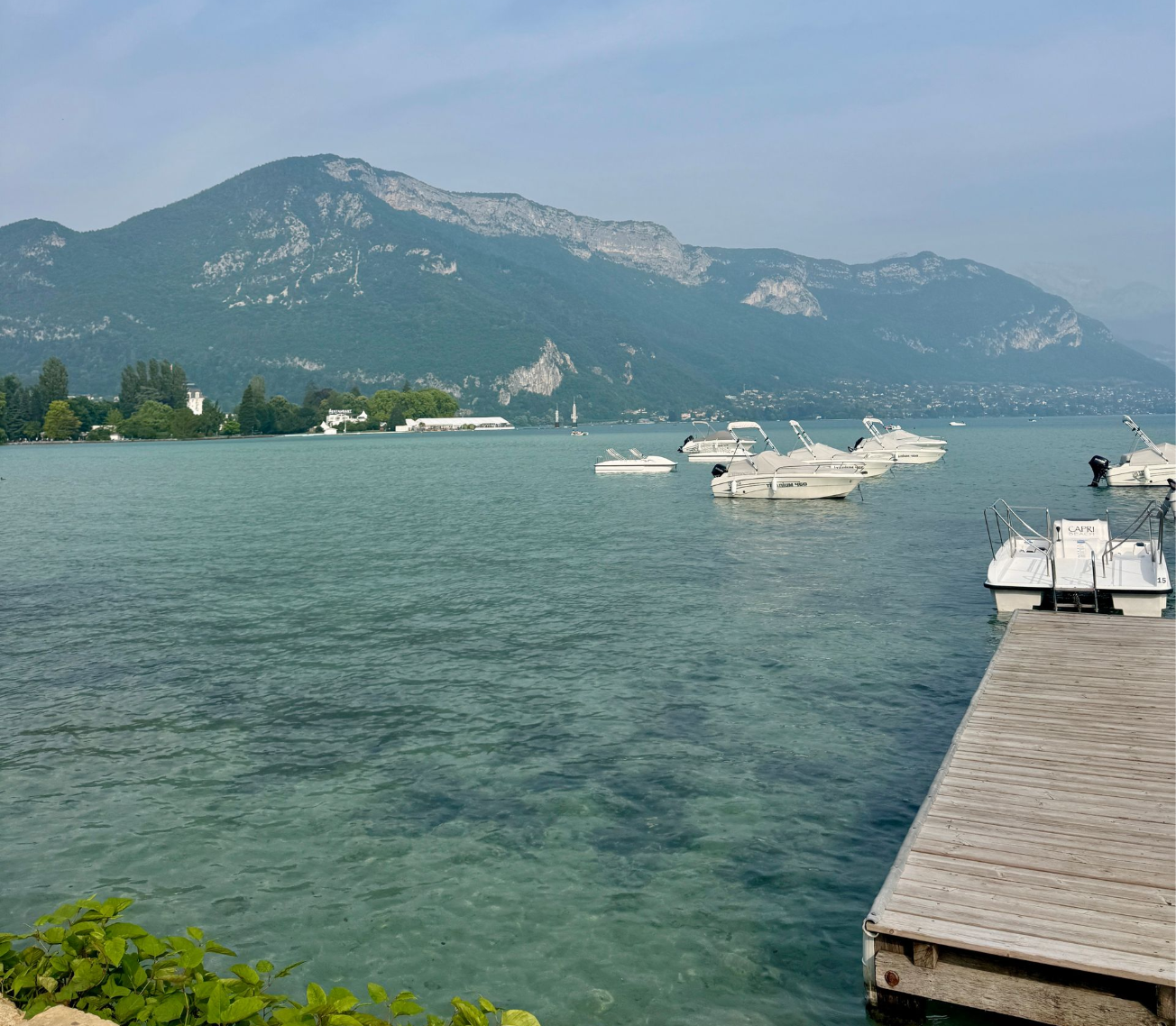 Boats on turquoise water, with a mountain backdrop, and a wooden dock in foreground.