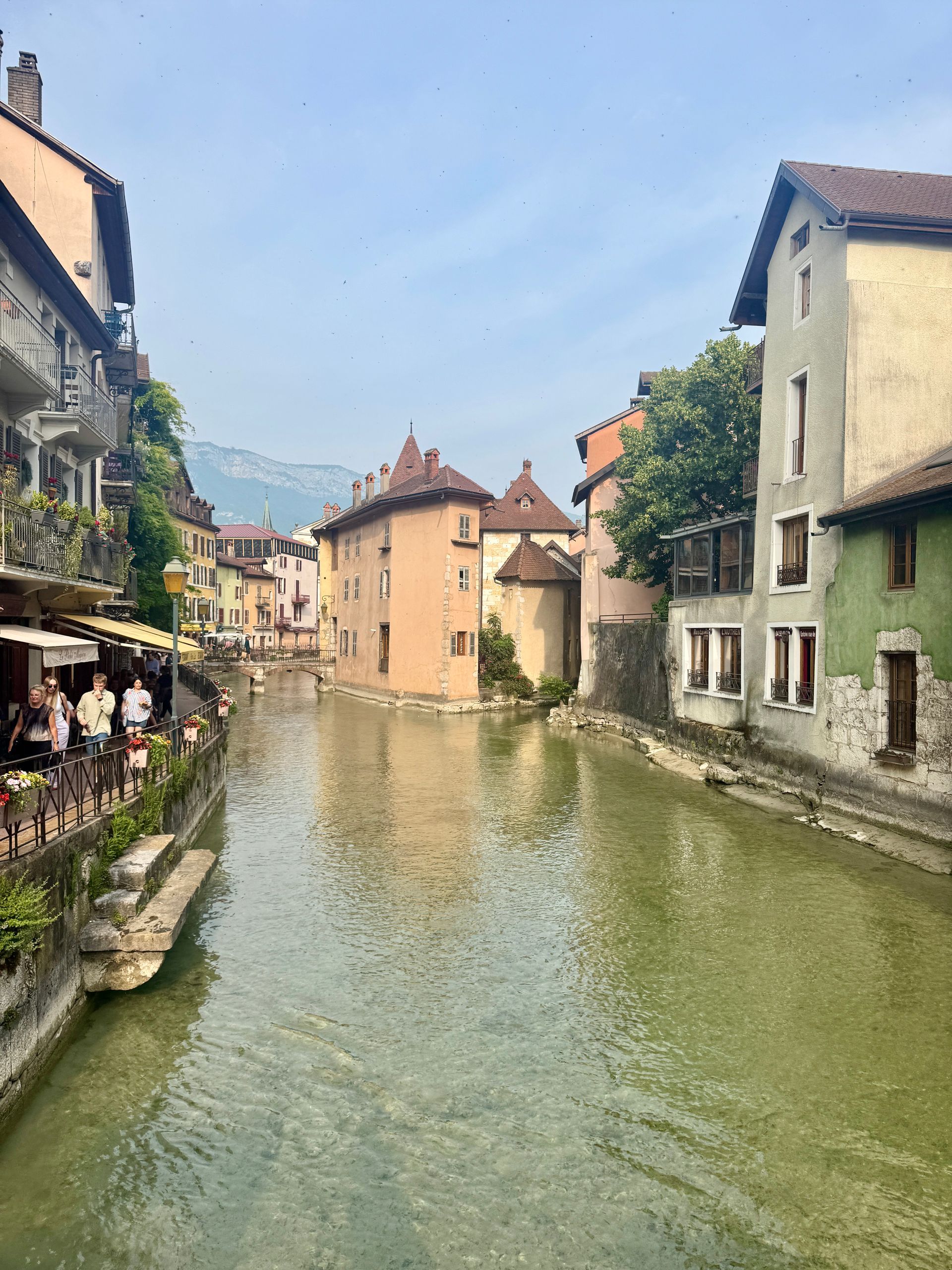 Canal in Annecy, France, with colorful buildings lining the water. People at outdoor restaurant.