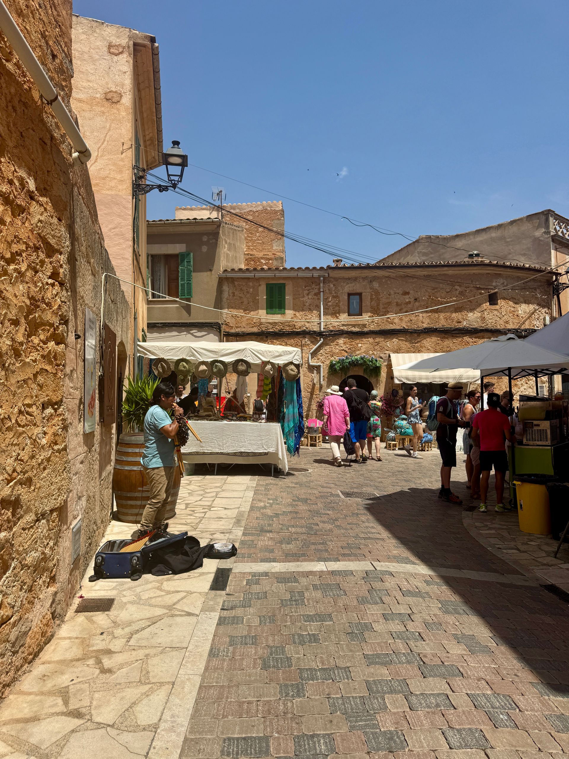 Man playing flute on cobblestone street with market stalls and people in Santanyí in Majorca, Spain.