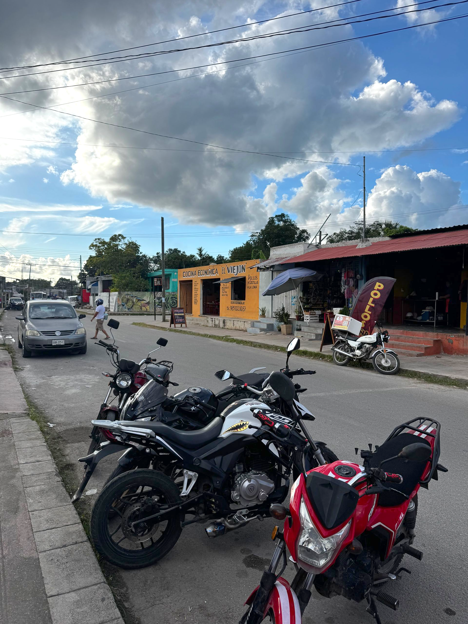 Motorcycles parked on a street in front of buildings under a cloudy blue sky.