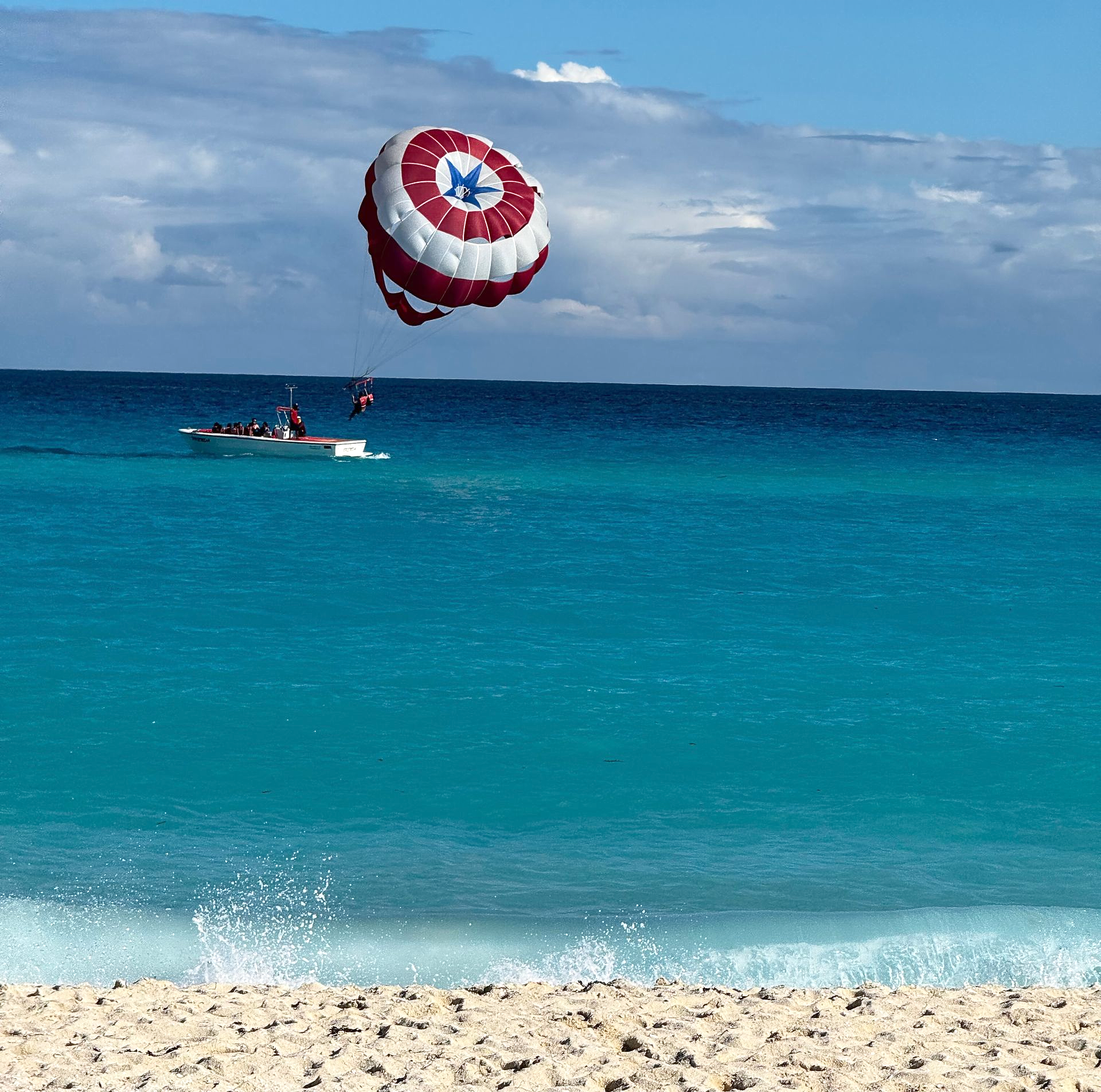 Parasailer with red and white design soaring over turquoise ocean, boat below.