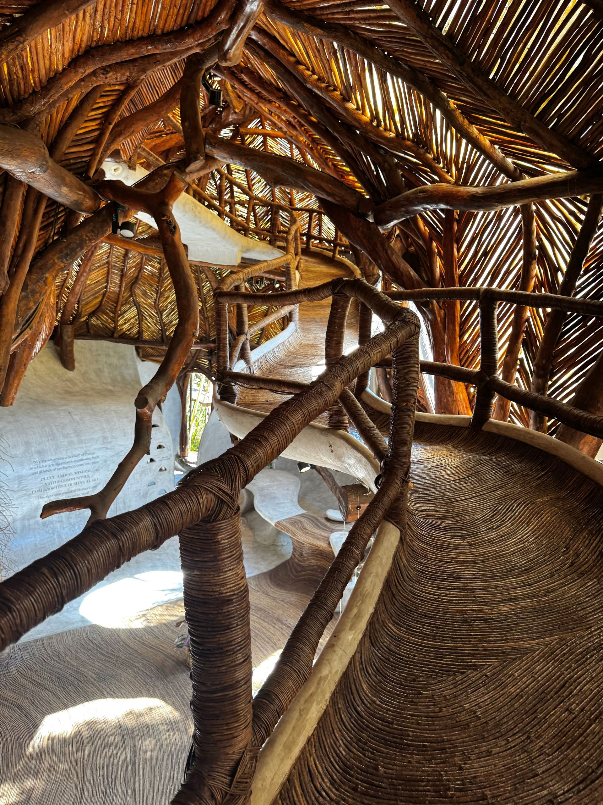Interior view of a rustic wooden structure with a winding walkway, featuring a thatched roof in Tulum, Mexico.