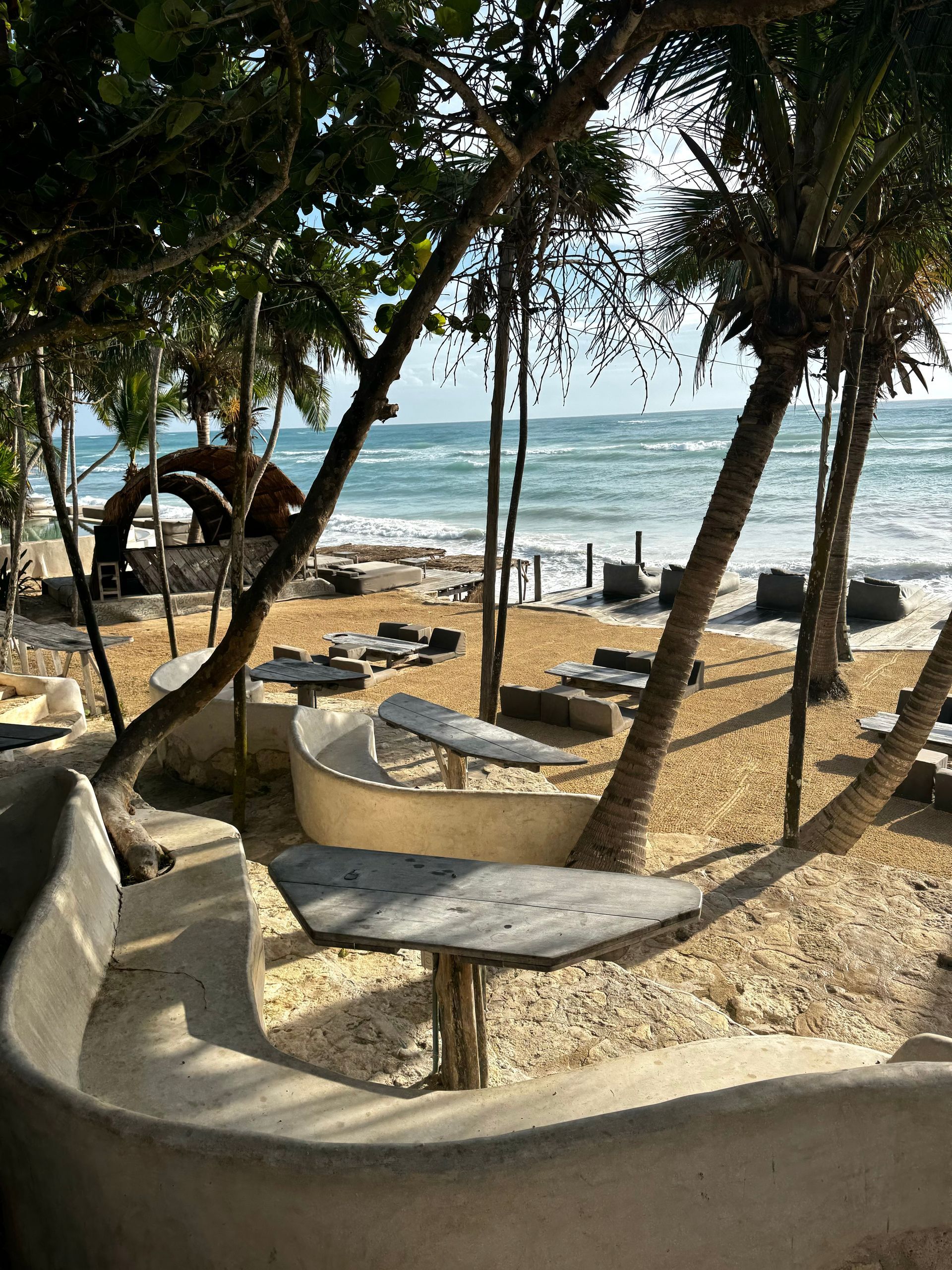 There are tables and chairs on the beach with a view of the ocean at Papaya Playa Beach Club in Tulum.