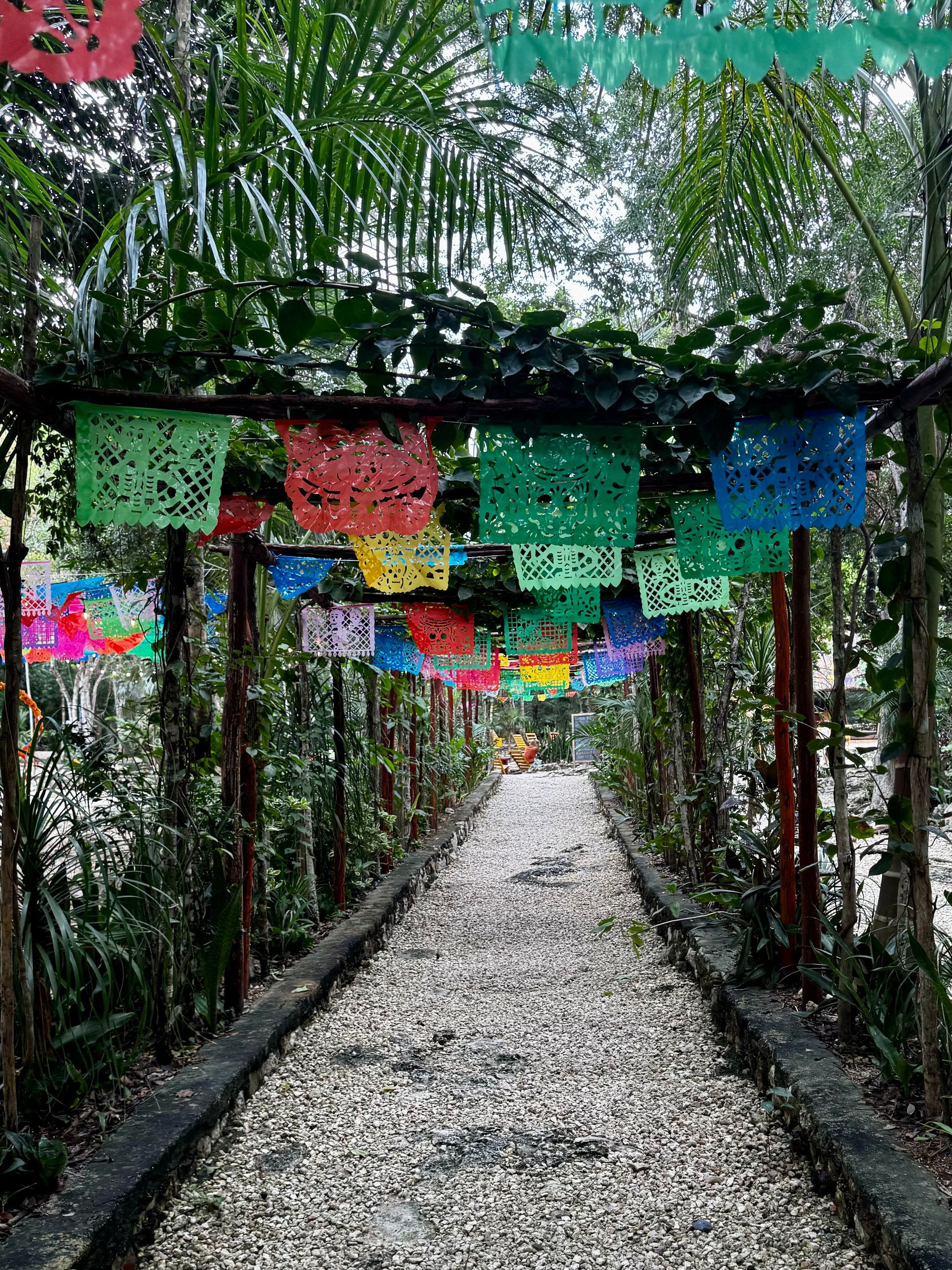 A path in the woods with colorful paper flags hanging from the trees at Cenote Calavera in Tulum, Mexico.