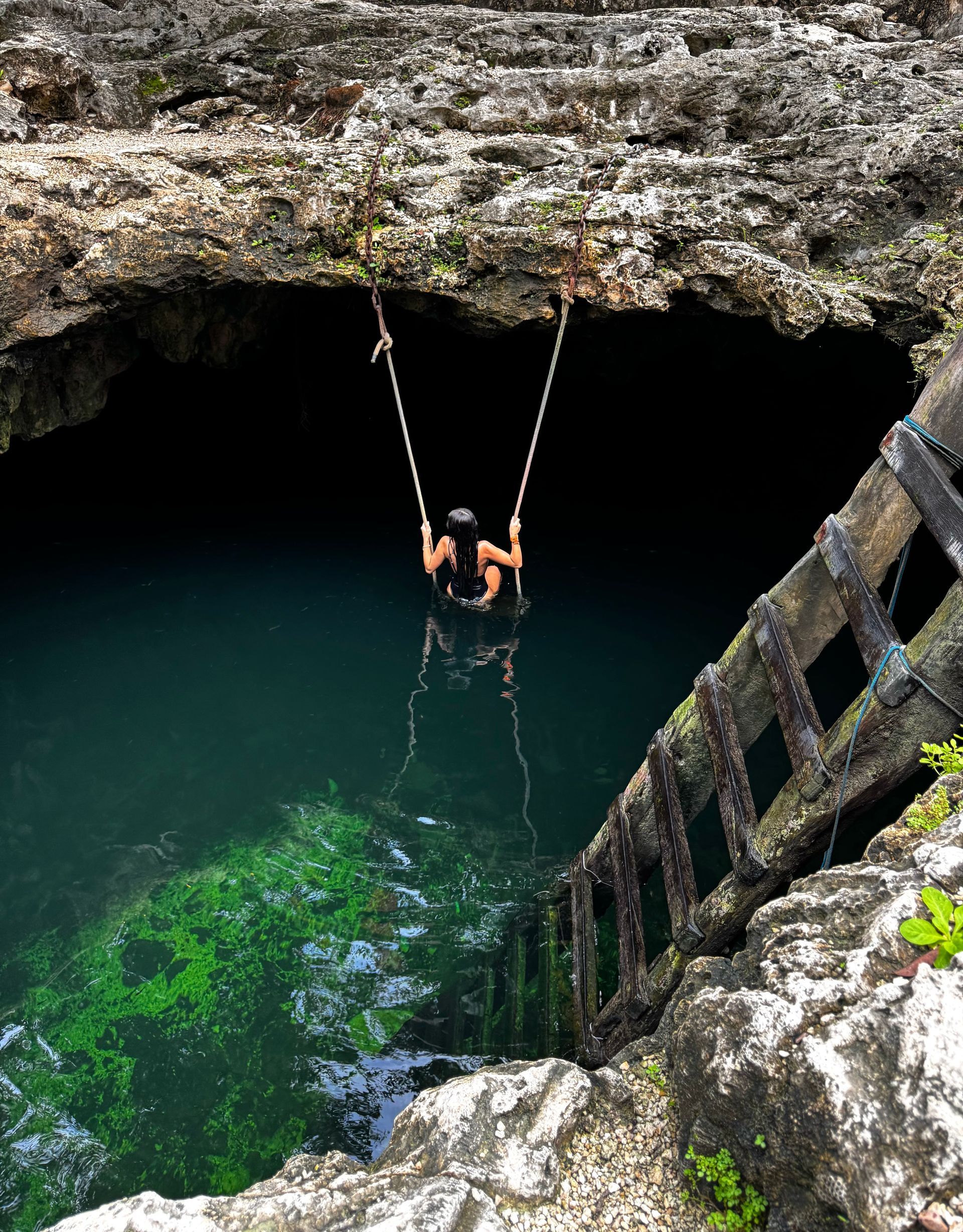A person is swinging from a swing in Cenote Calavera in Tulum, Mexico.