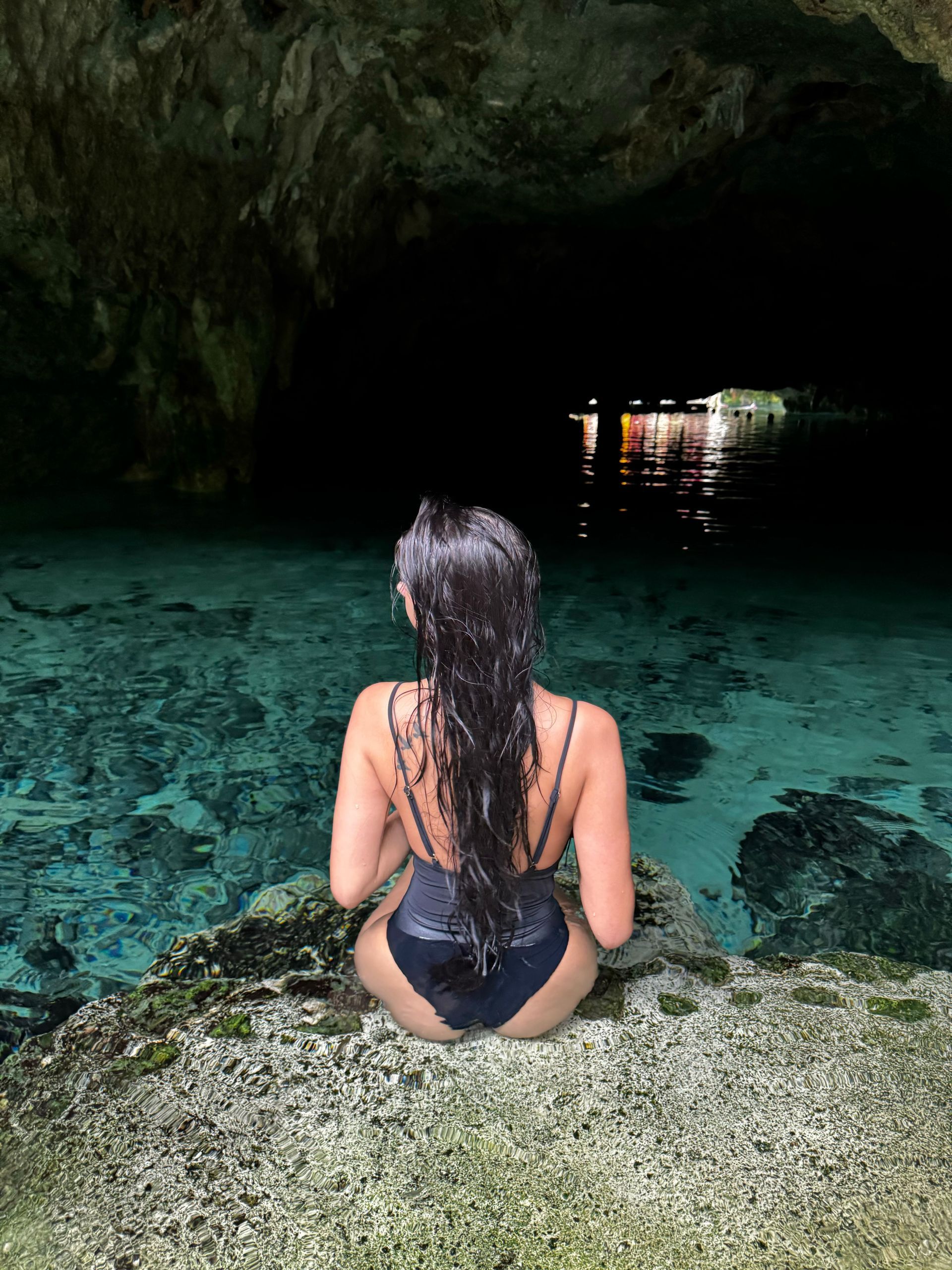 A woman in a swimsuit is sitting on a rock in a cave at Gran Cenote in Tulum, Mexico.