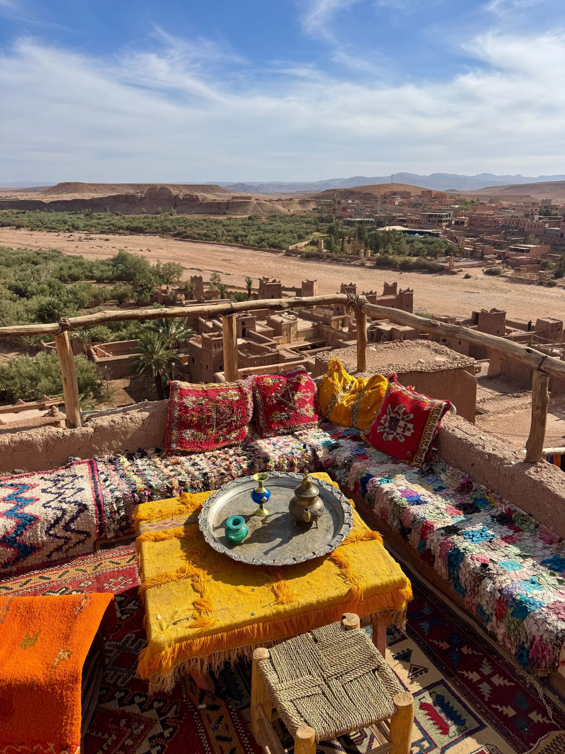 Rooftop seating area overlooking a desert landscape. Colorful cushions and rug surround a low table with tea set.