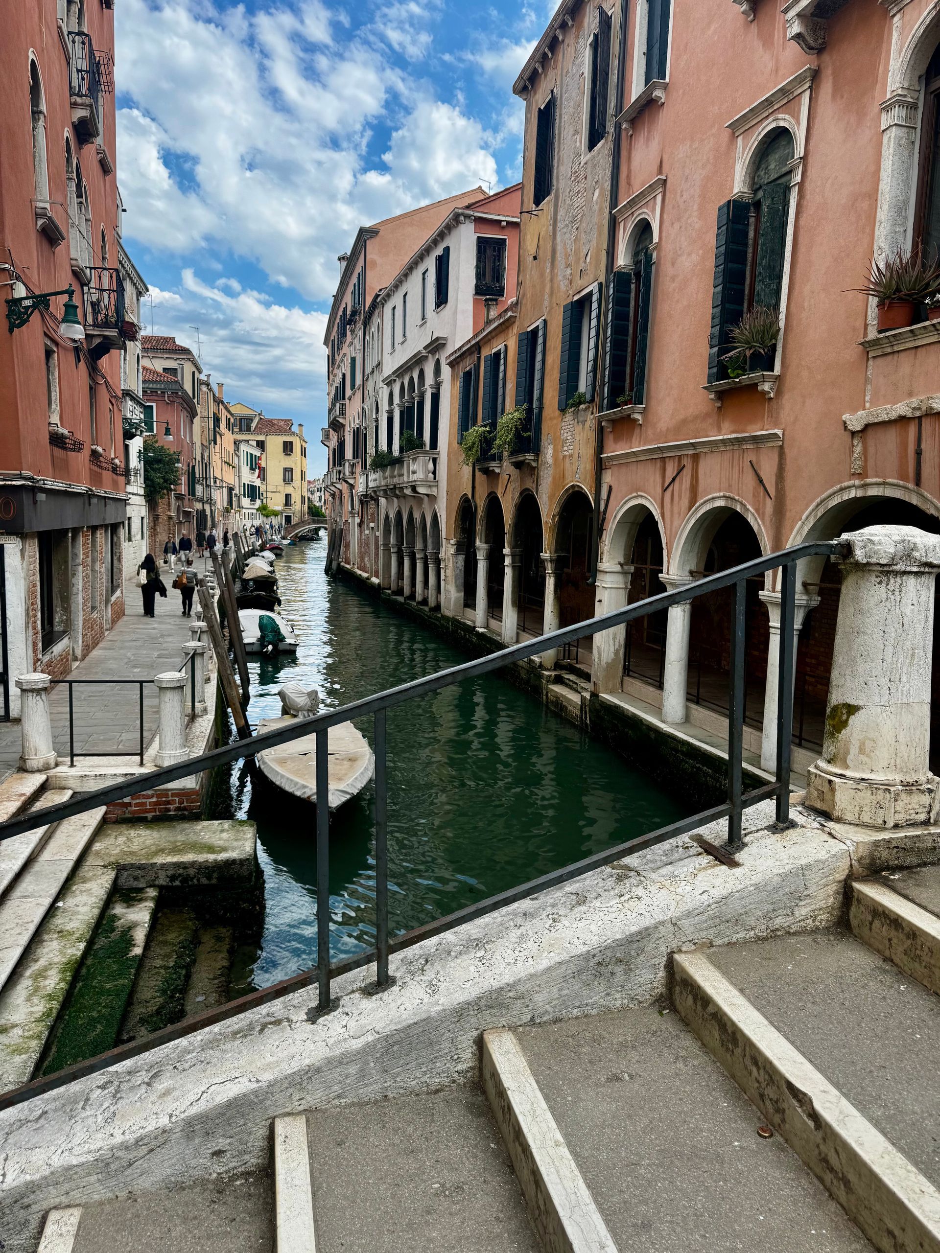 Venice canal scene: buildings line a waterway; a boat floats. Steps and a railing are in the foreground.