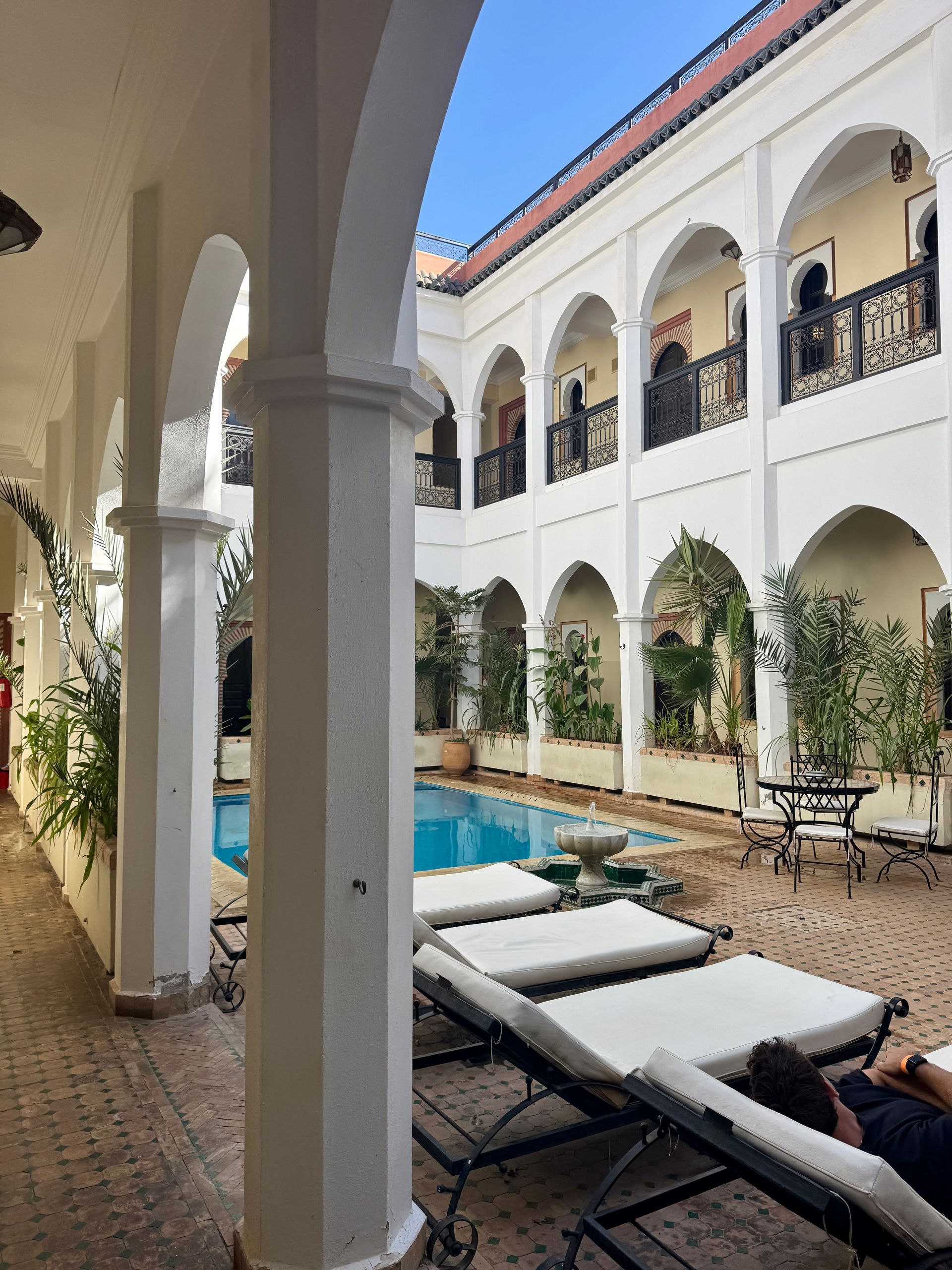 Riad with pool and lounge chairs, arched walkways, white walls, and blue sky in, Marrakesh, Morocco