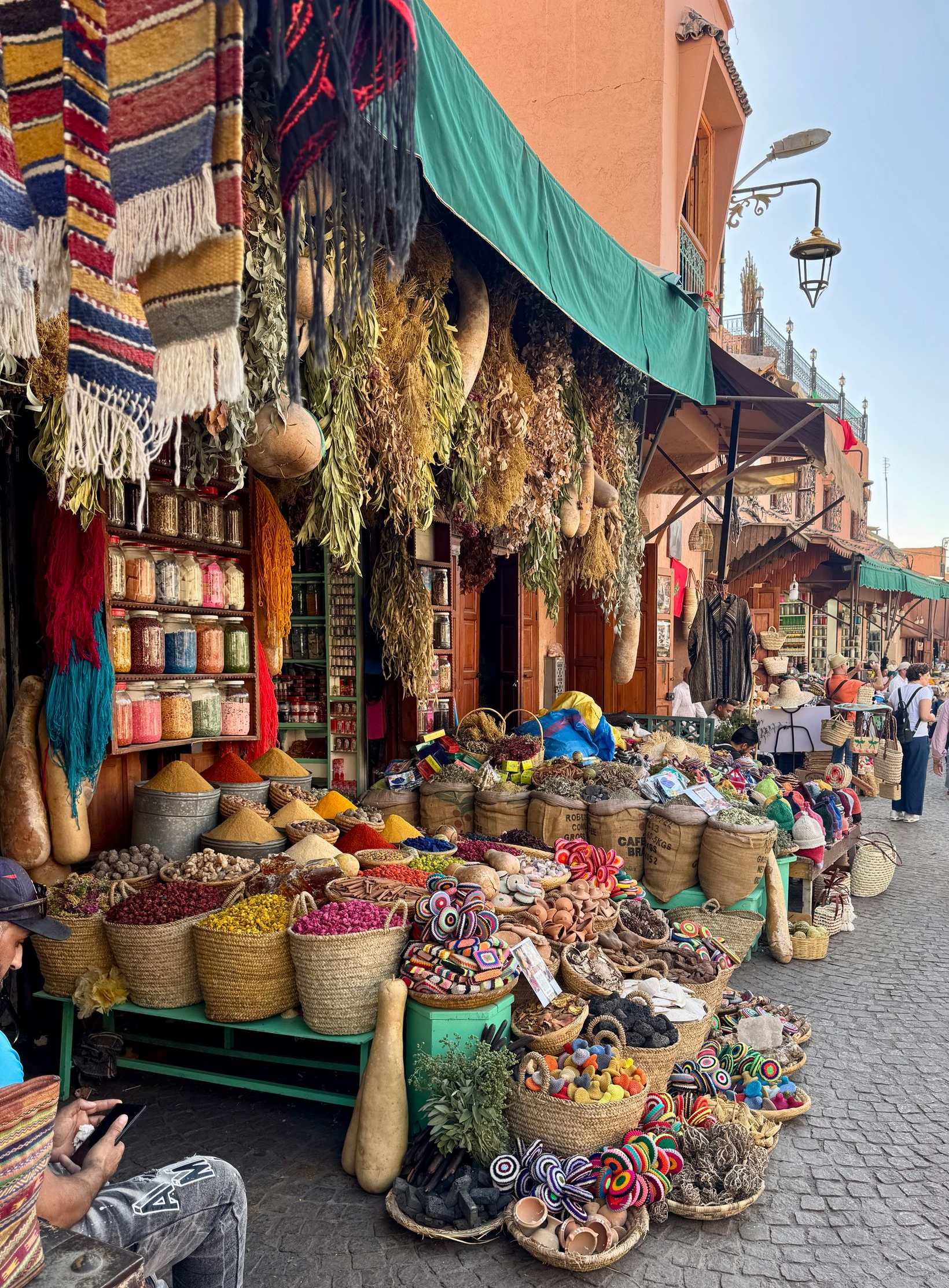 Spice market stall in Marrakech, Morocco. Colorful baskets overflowing with spices, herbs, and flowers under a green awning.