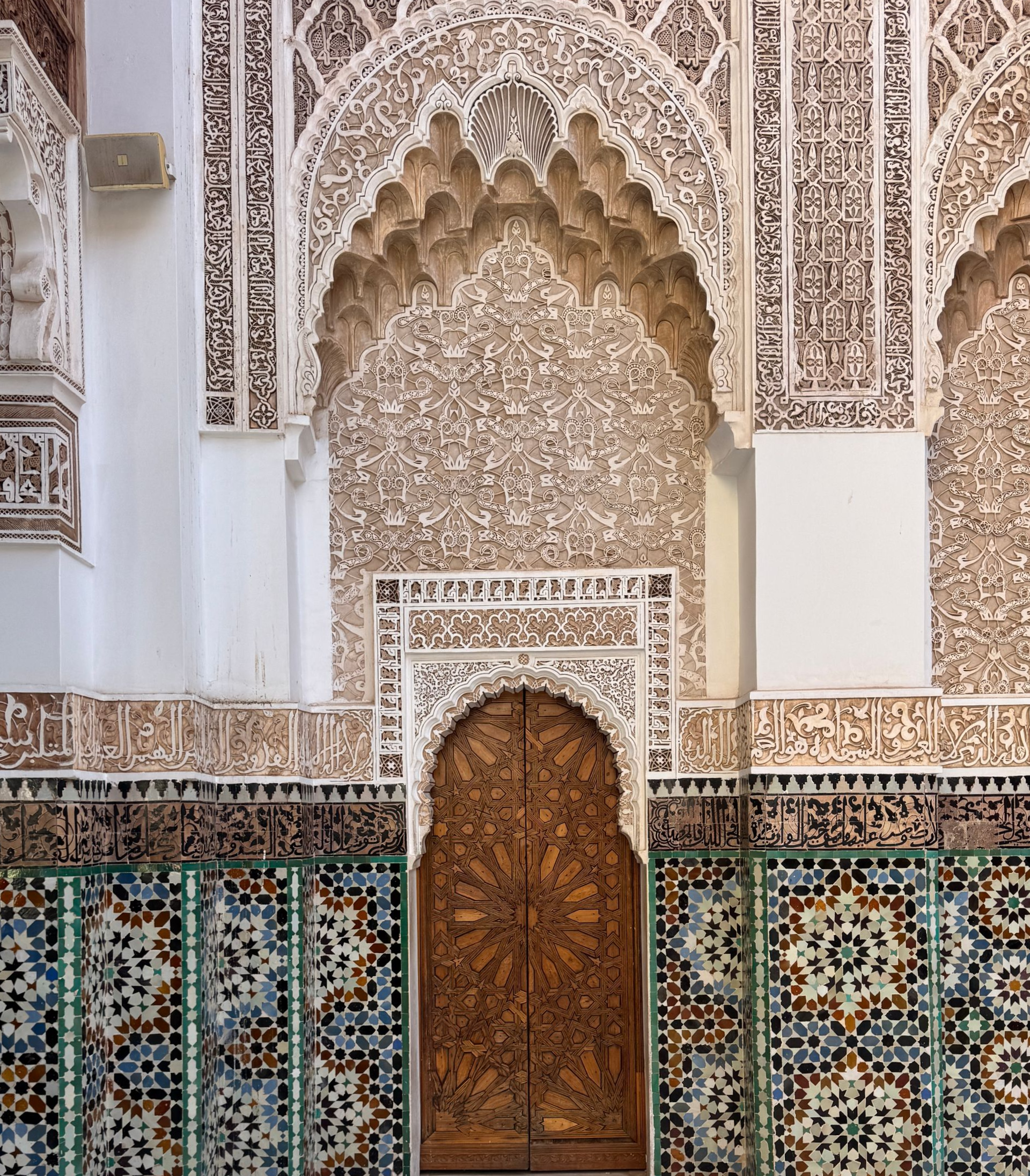 Ornate doorway with carved wood doors, surrounded by patterned tiles and intricate plasterwork.