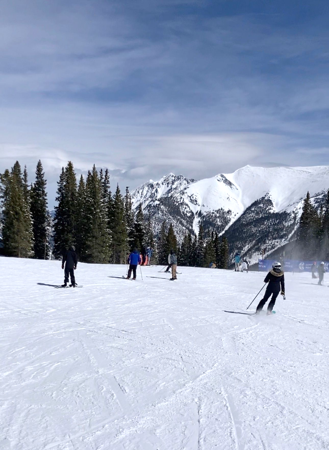 Skiers on a snow-covered mountain slope with a backdrop of snow-capped peaks and blue sky.