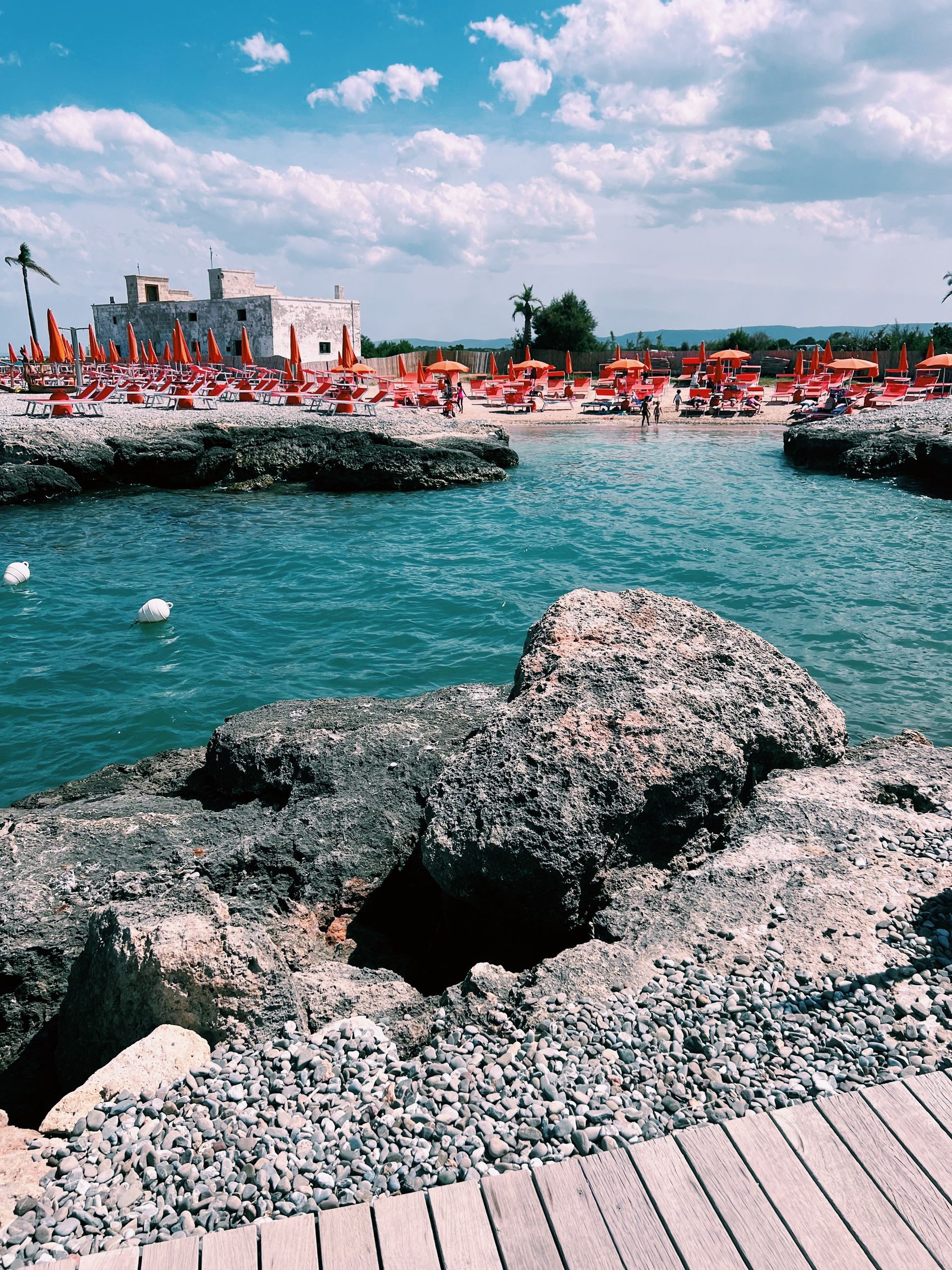A beach with orange umbrellas and rocks in the foreground in Puglia, Italy.