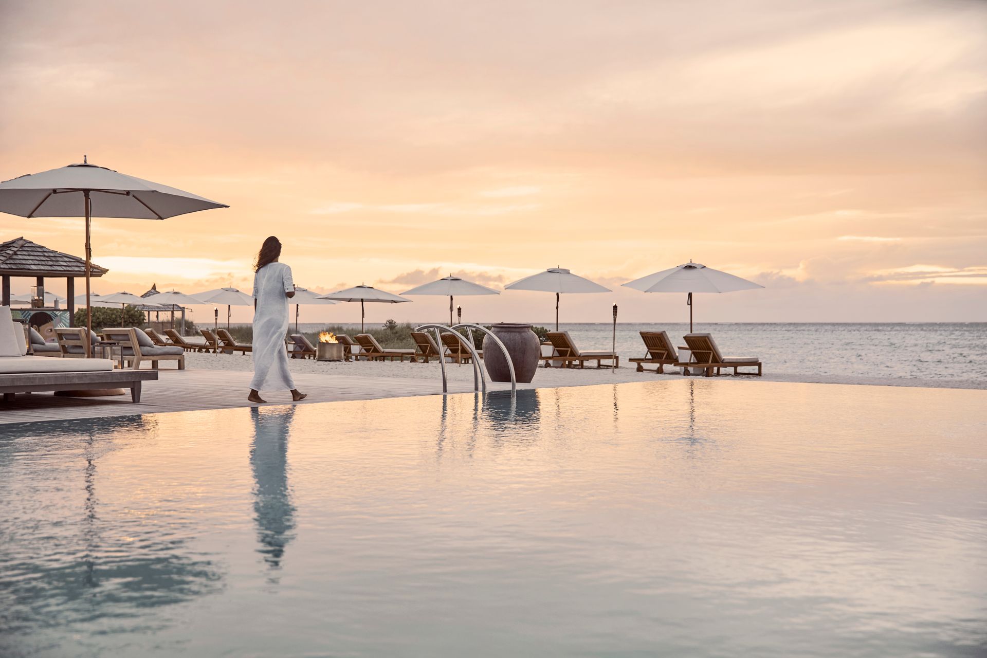A woman is walking along the edge of Como Hotel's infinity pool at sunset in Turks & Caicos.