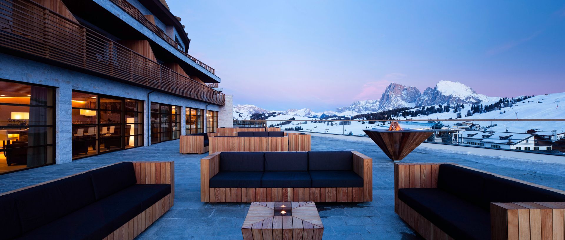 A patio with a couch and a table in front of a building with the Italian dolomites in the background at Como Hotel.
