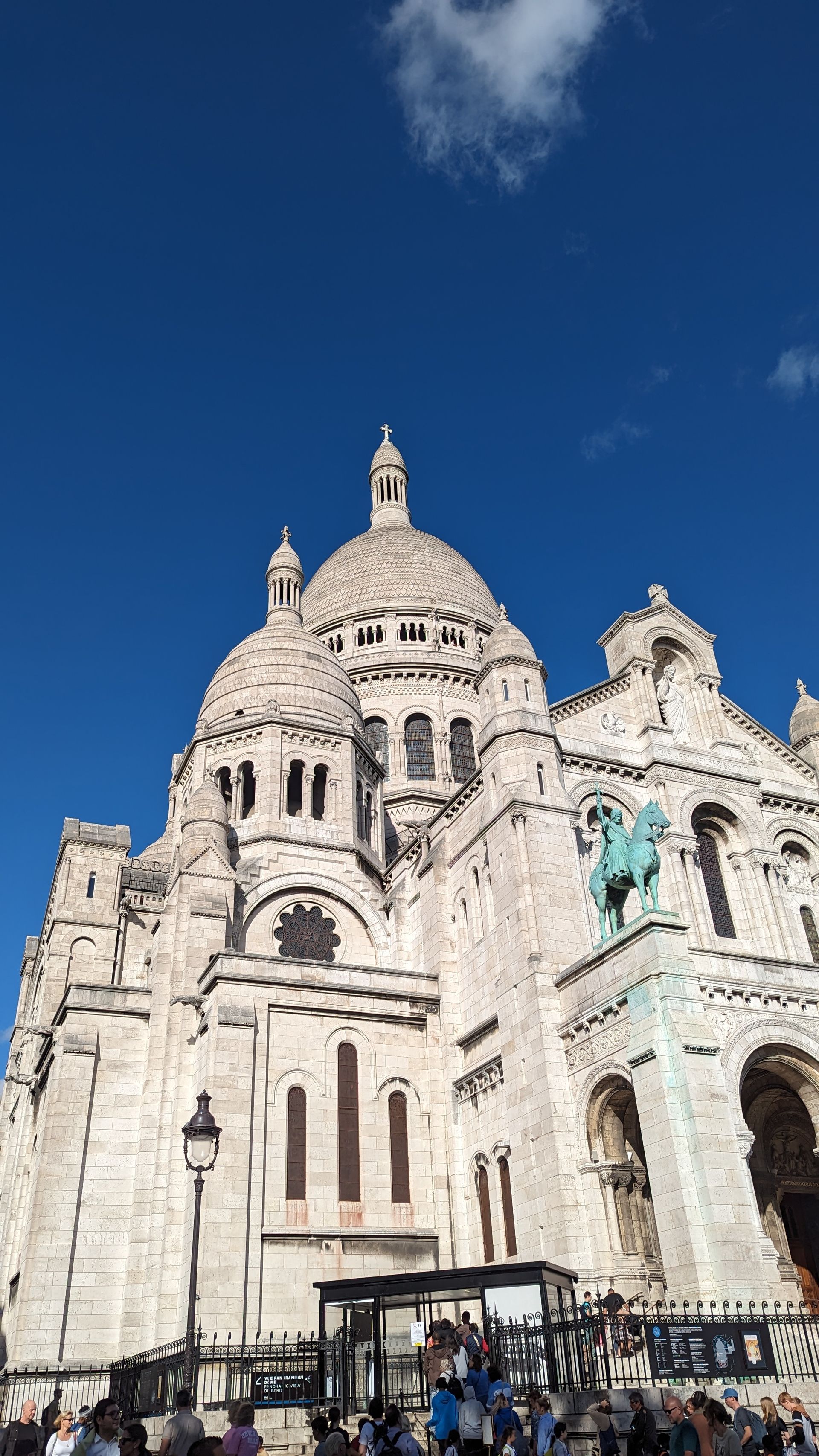 Sacré-Cœur Basilica, Paris, seen from below against a bright blue sky. Stone building with a large dome.