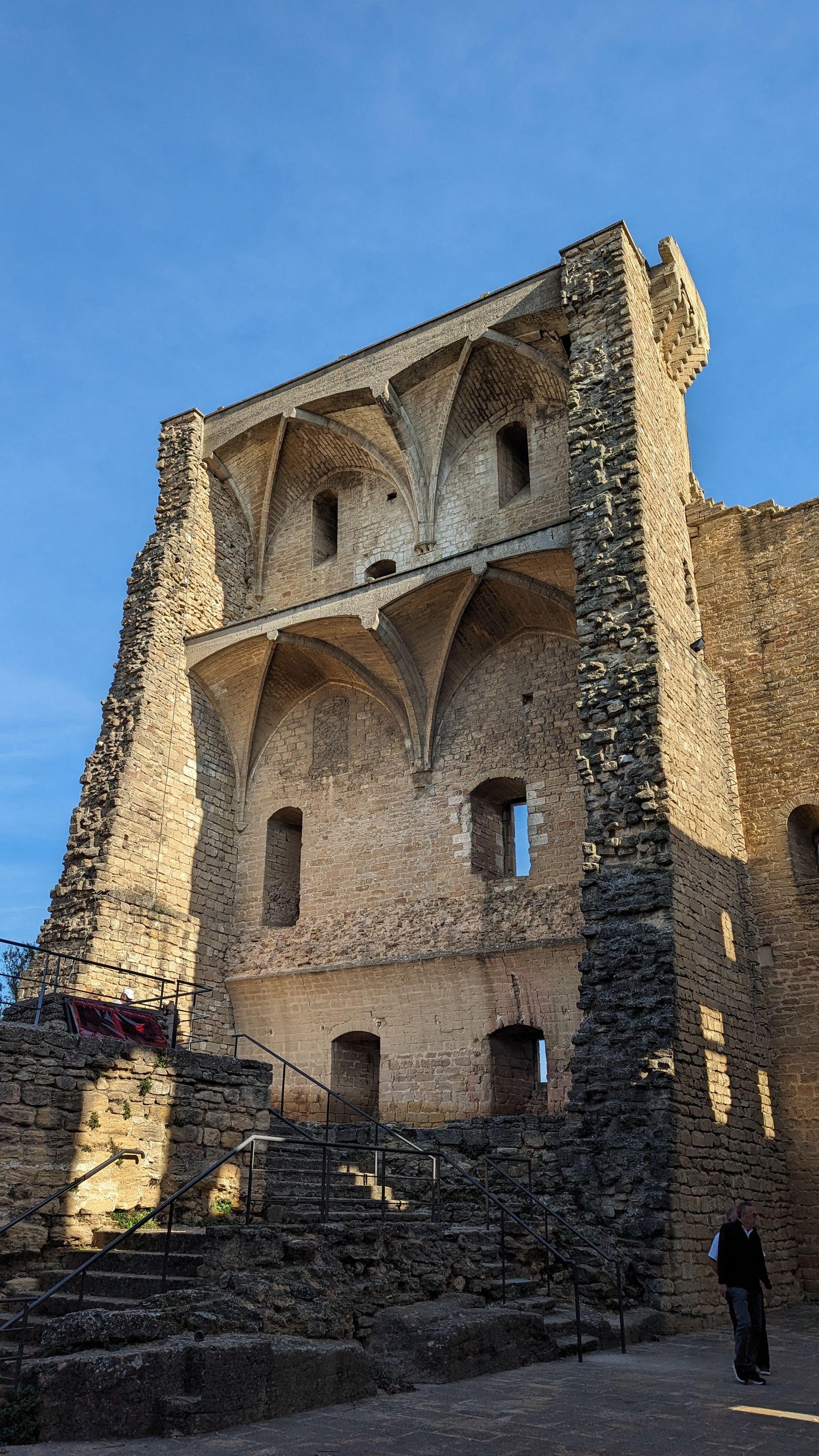 Stone castle ruin with arched vaults, steps, and a person walking in sunlight.