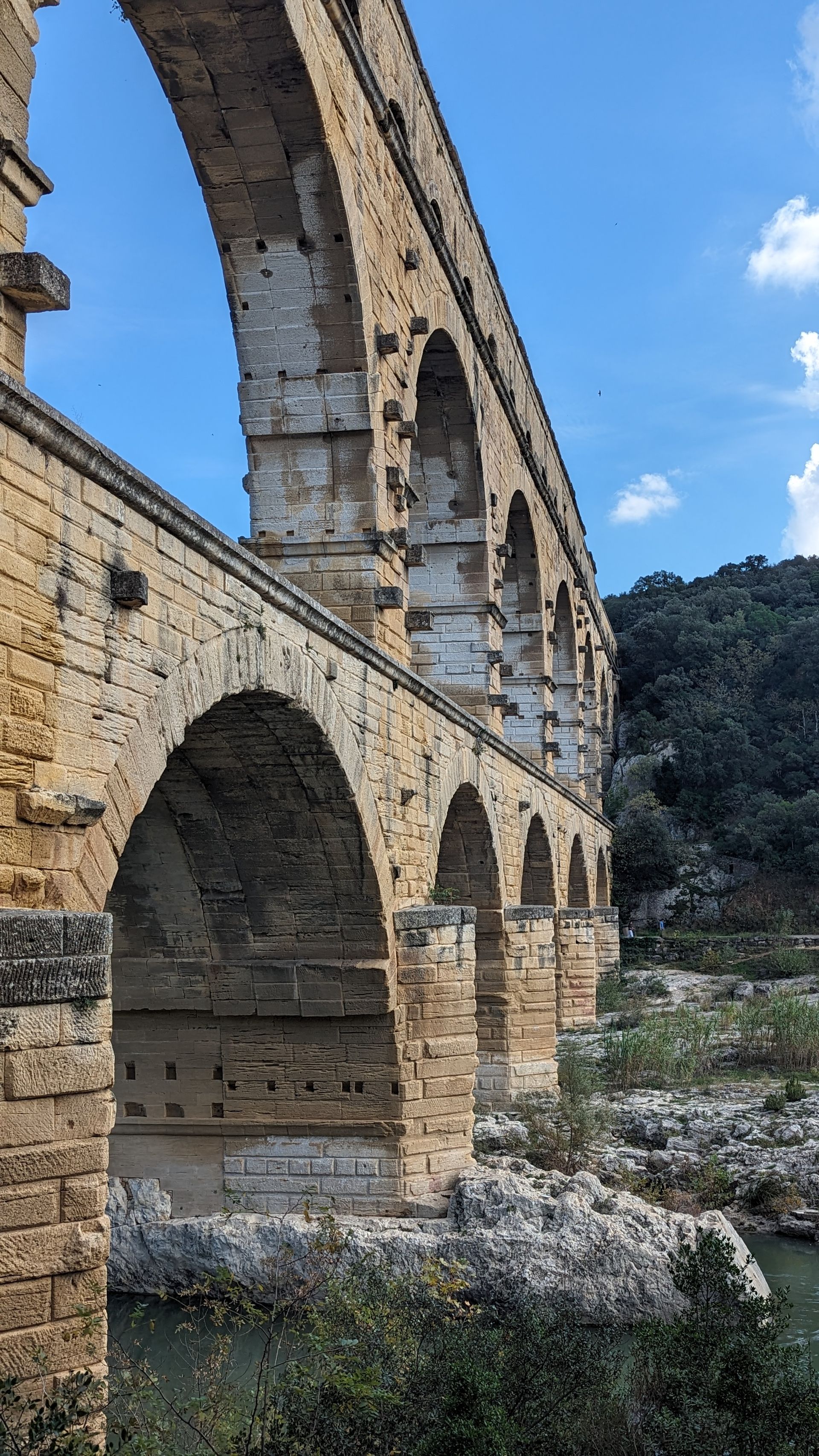 Stone Roman aqueduct arches against a blue sky, spanning a river.
