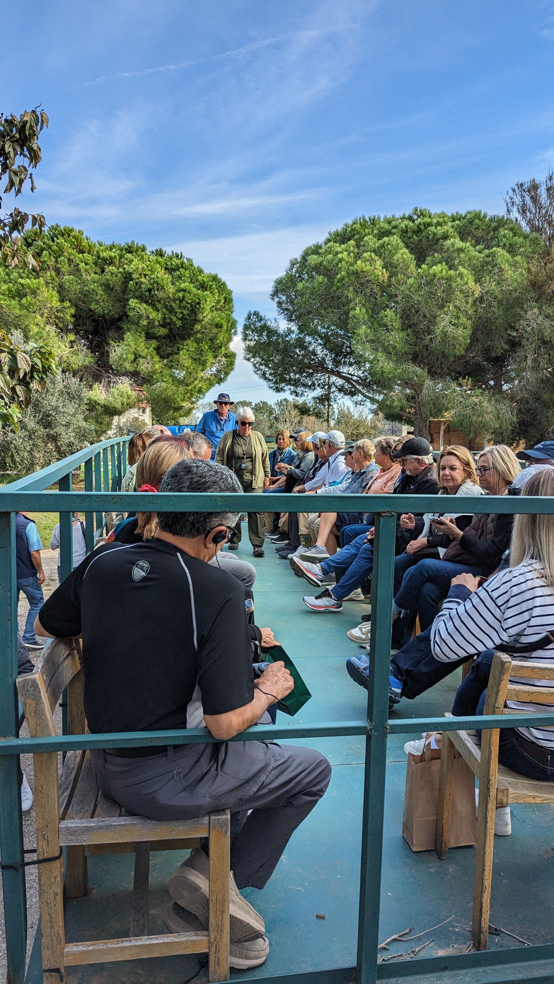 People seated on a wagon, likely on a tour, under a blue sky, surrounded by trees.