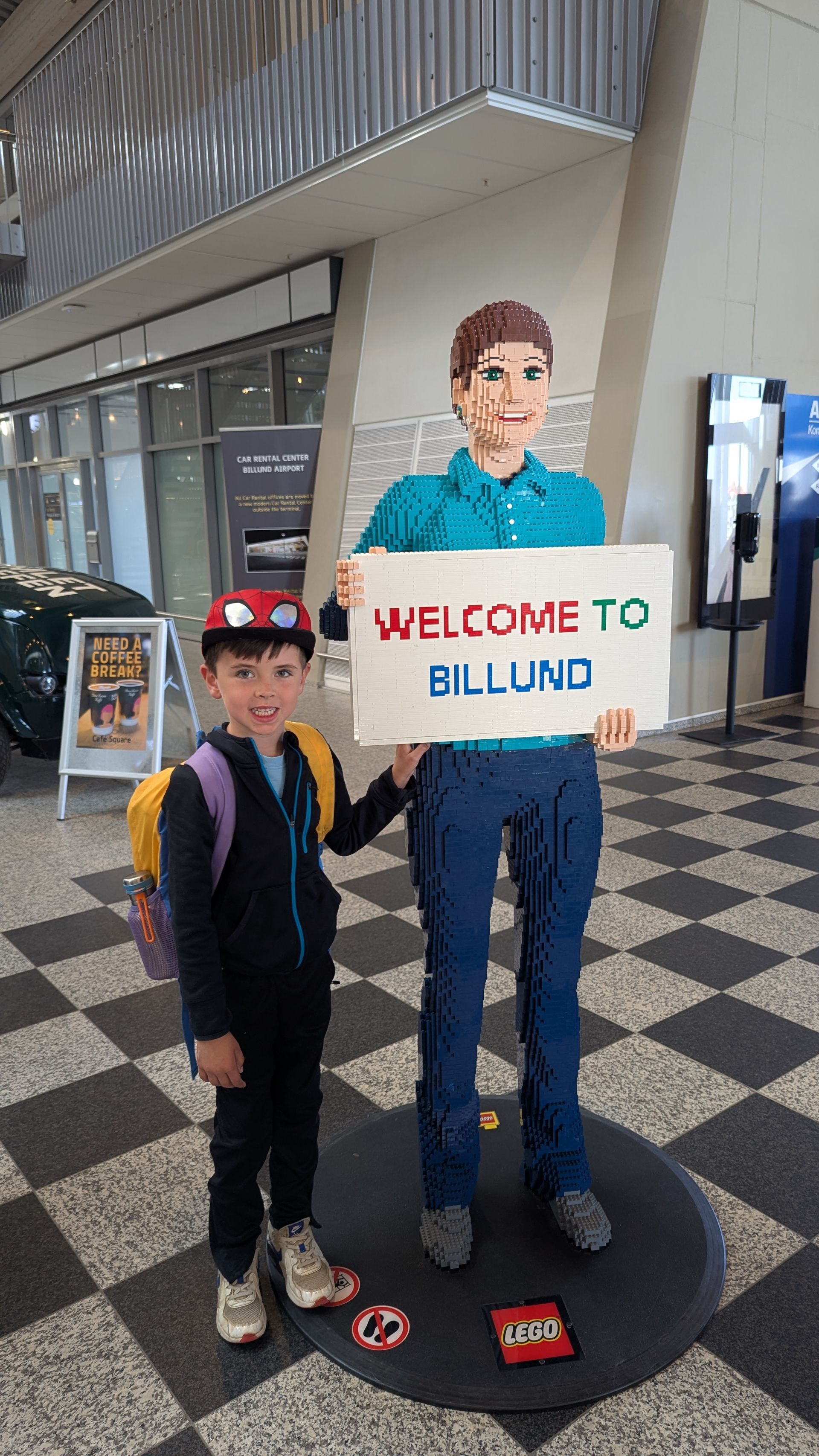 Boy with backpack stands next to a Lego statue holding a