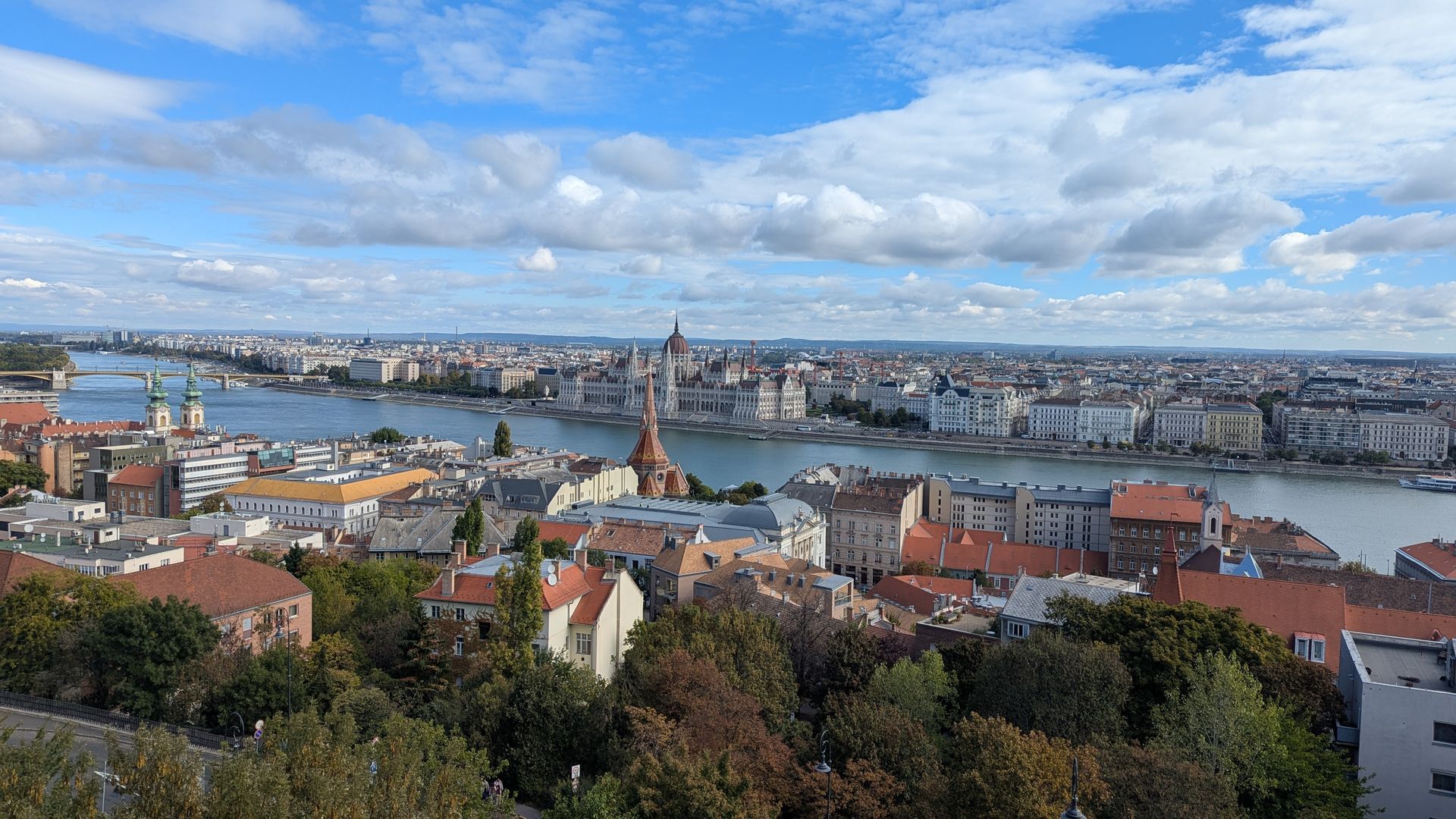 Cityscape view with river, buildings, and blue sky with clouds.
