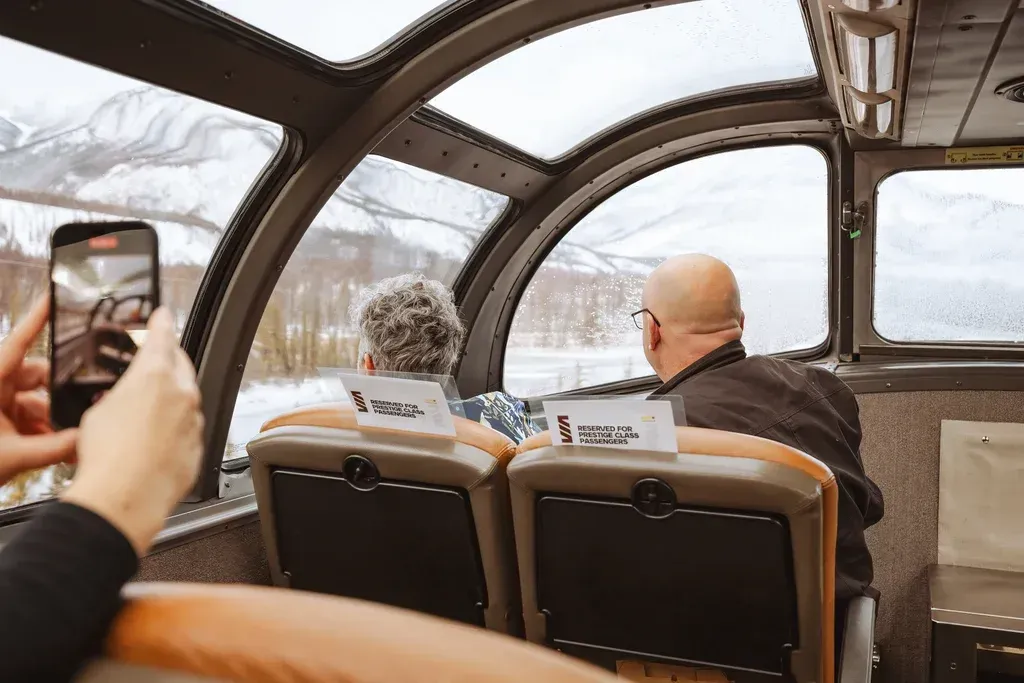 A person is taking a picture of two people sitting on a Via Rail train.