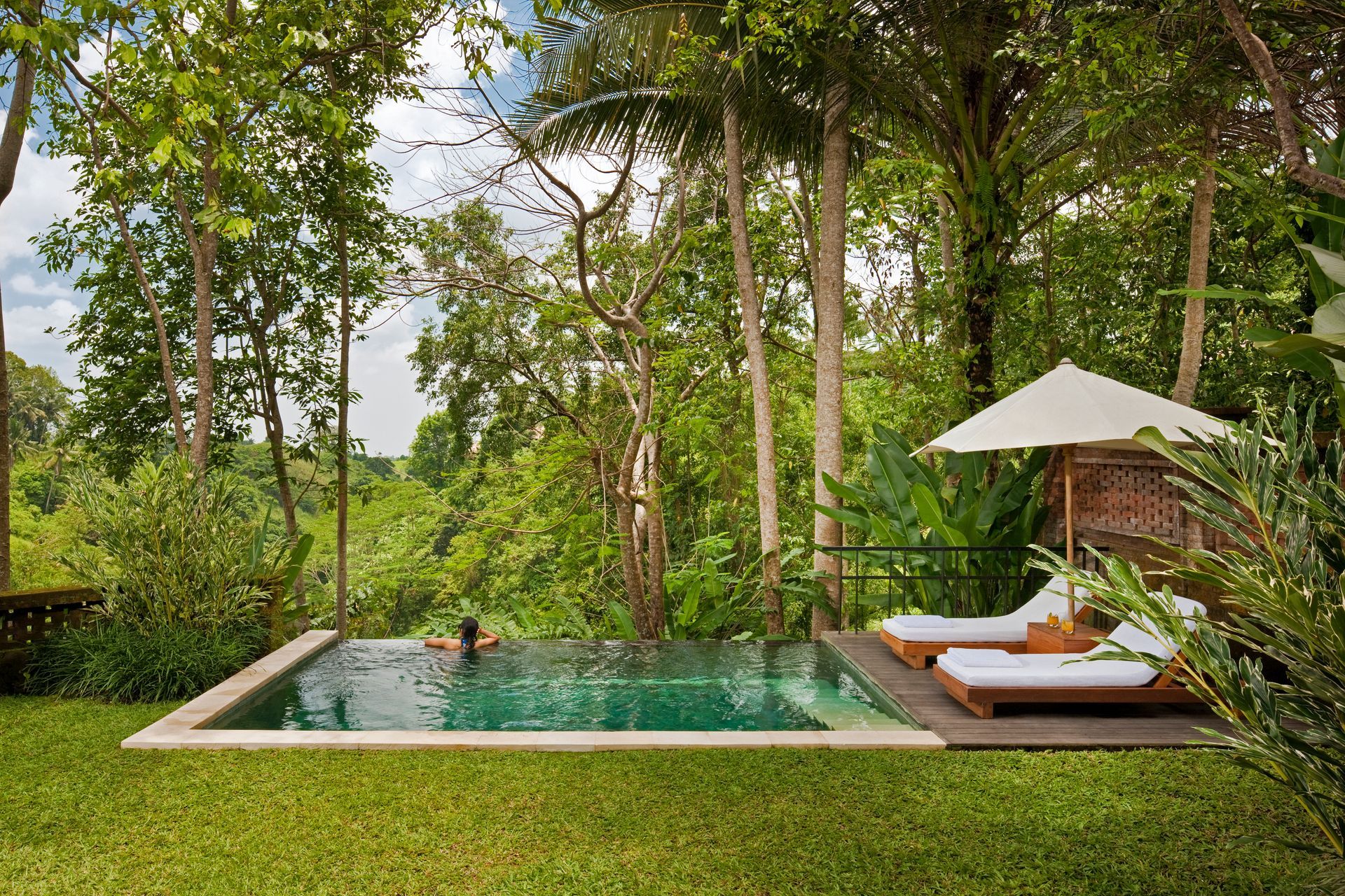 A man is swimming in a swimming pool in the middle of a lush green forest in Ubud, Bali at Como Hotel. 