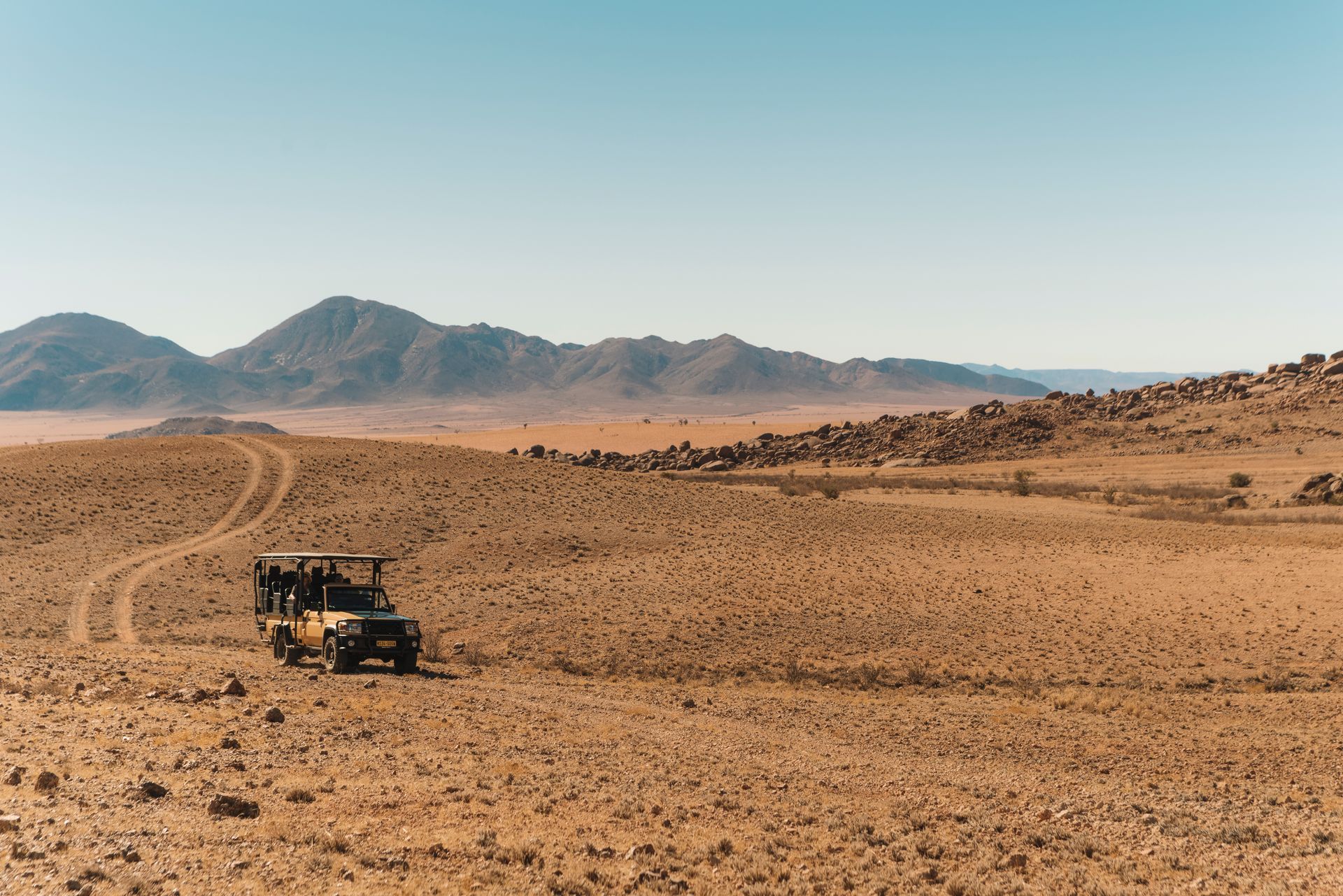 A jeep is driving through a desert with mountains in the background in Namibia, Africa.